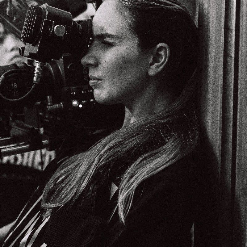 Black and white photo of a woman looking through a film camera on a movie set.