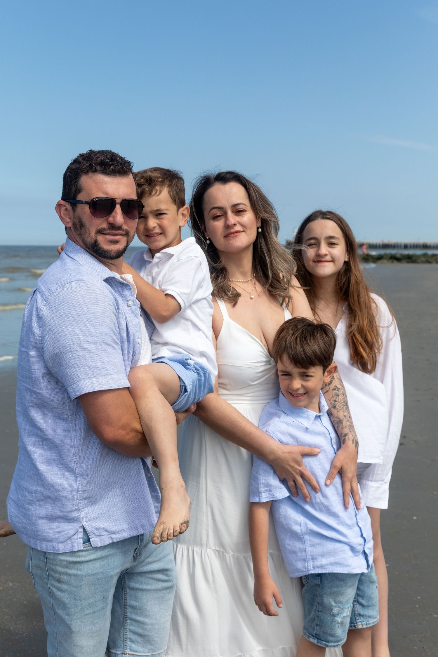 A happy family of five poses together on a sunny beach with ocean in the background. photography brussels