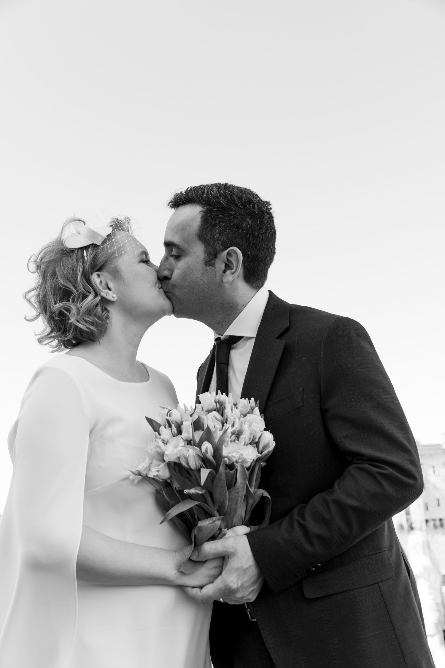 Black and white photo of a bride and groom kissing while holding a bouquet of tulips on their wedding day.