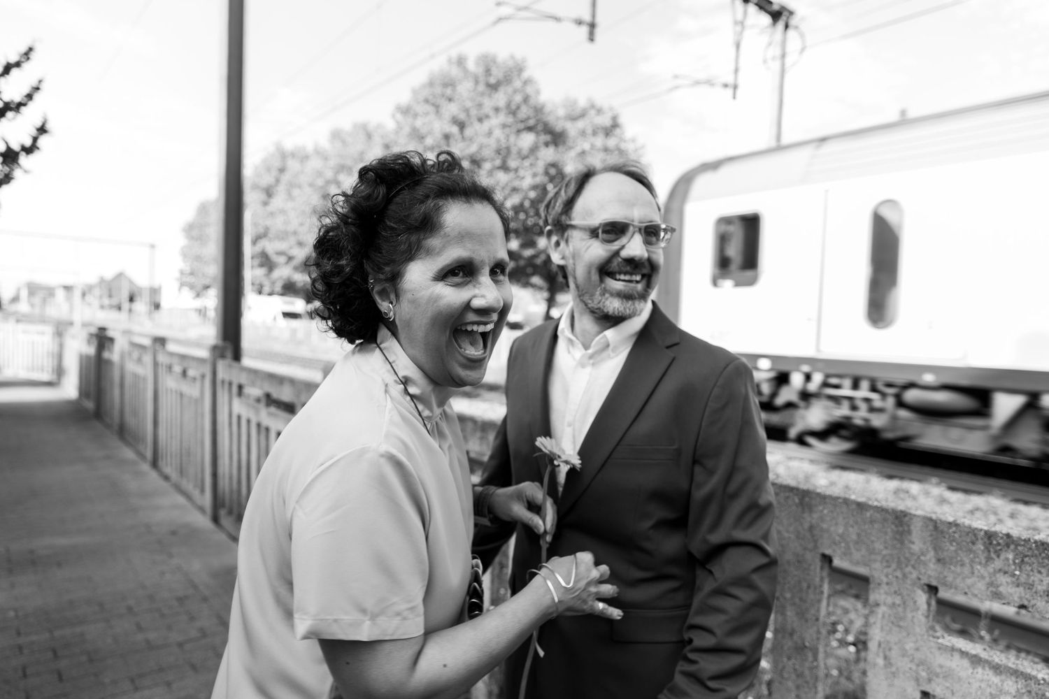 Laughing couple in black and white photo at a train station platform.