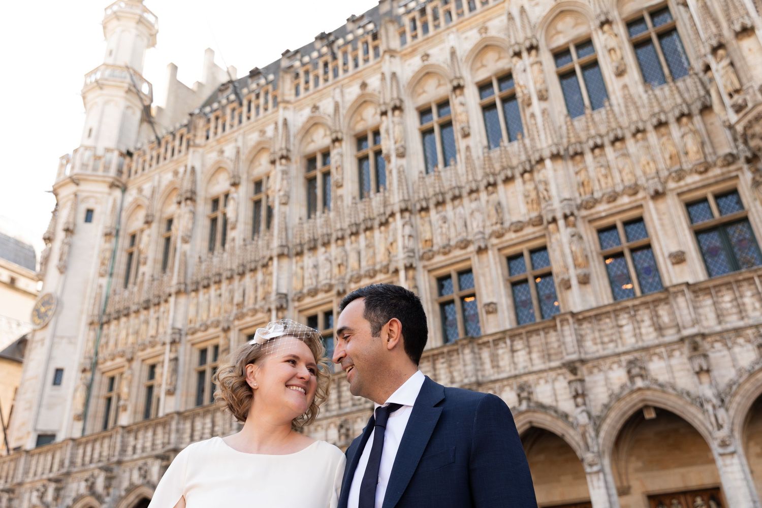 Bride and groom smiling at each other in front of an ornate Gothic building in Brussels Grand Place.