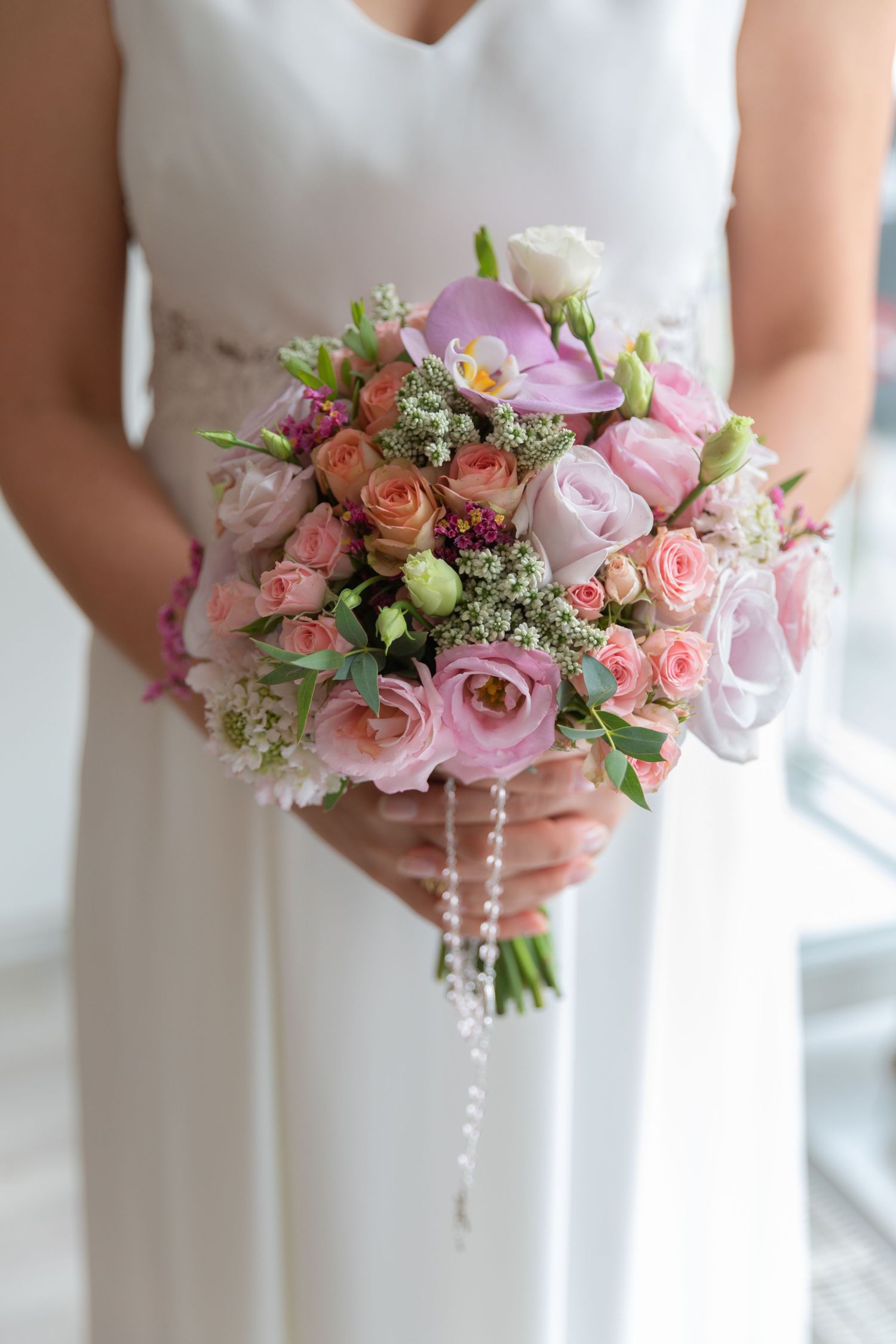 Bride in white gown holding elegant pink and peach rose bridal bouquet with pearl strand accents.
