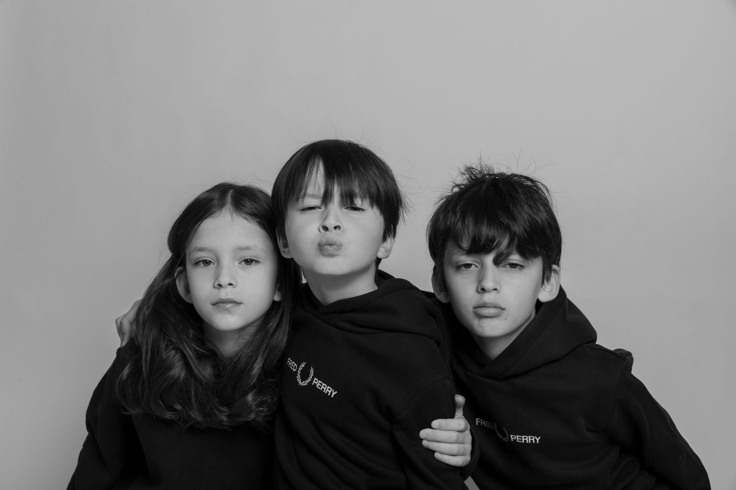 Black and white portrait of three children in dark hoodies posing together against a light background. photography brussels