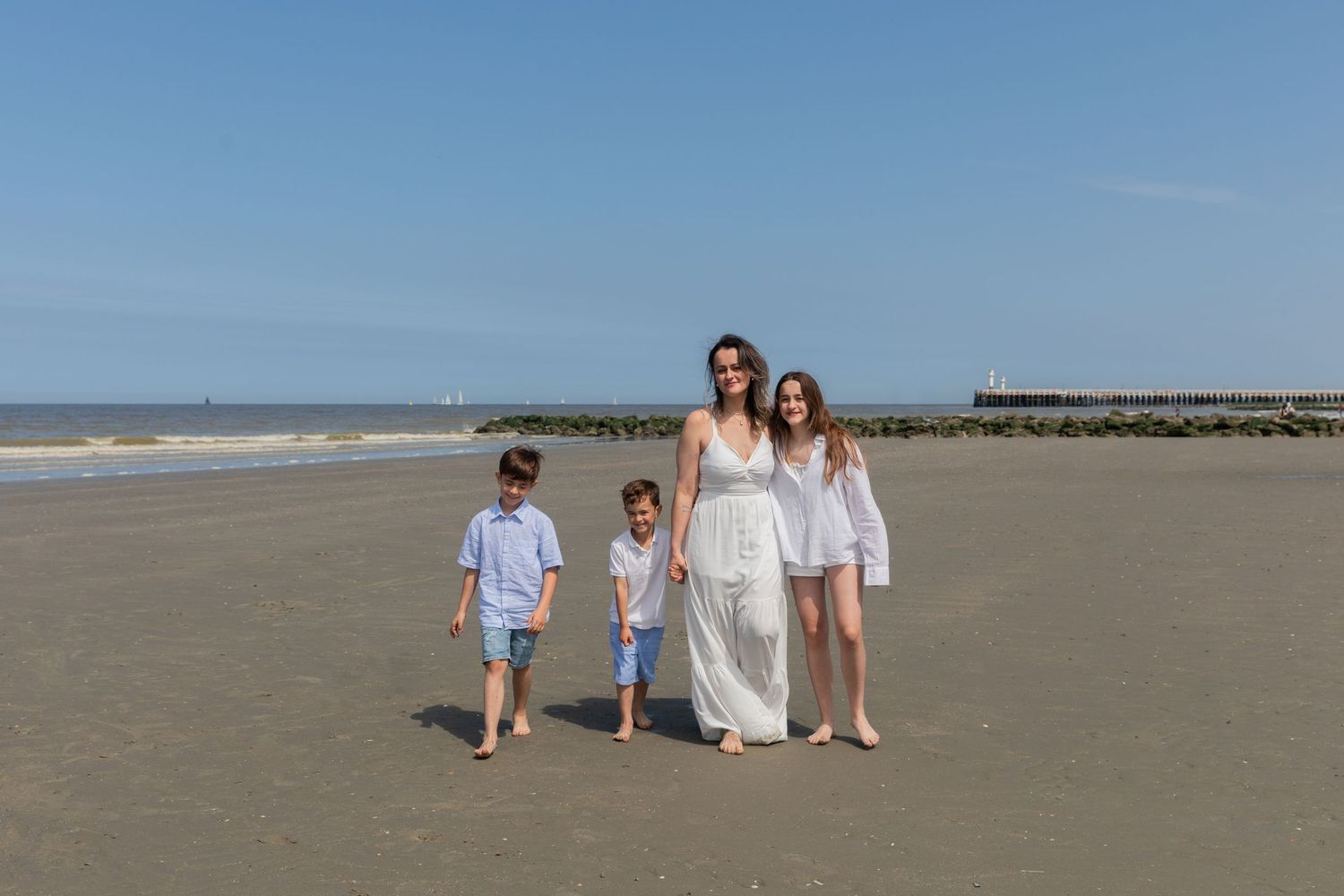 A mother walks on the beach with her three children on a clear sunny day. photography brussels