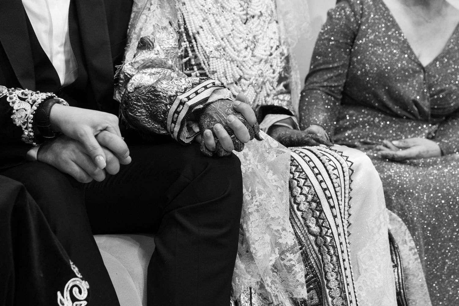 Black and white photo of hands held together at a South Asian wedding ceremony, showcasing intricate henna and traditional attire.