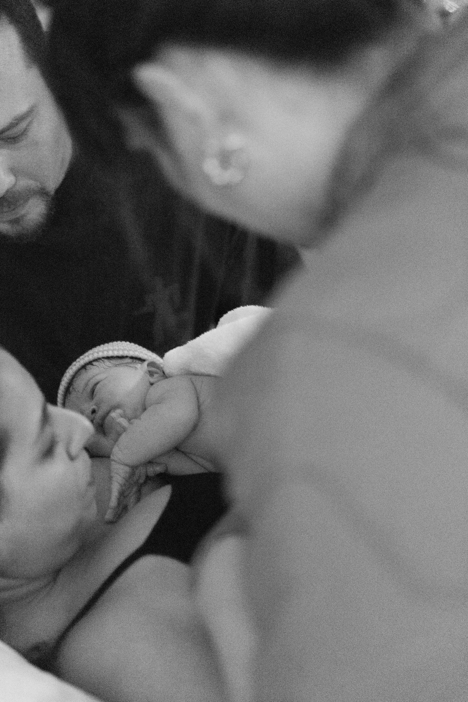 Black and white photo of new parents tenderly holding their newborn baby shortly after birth.