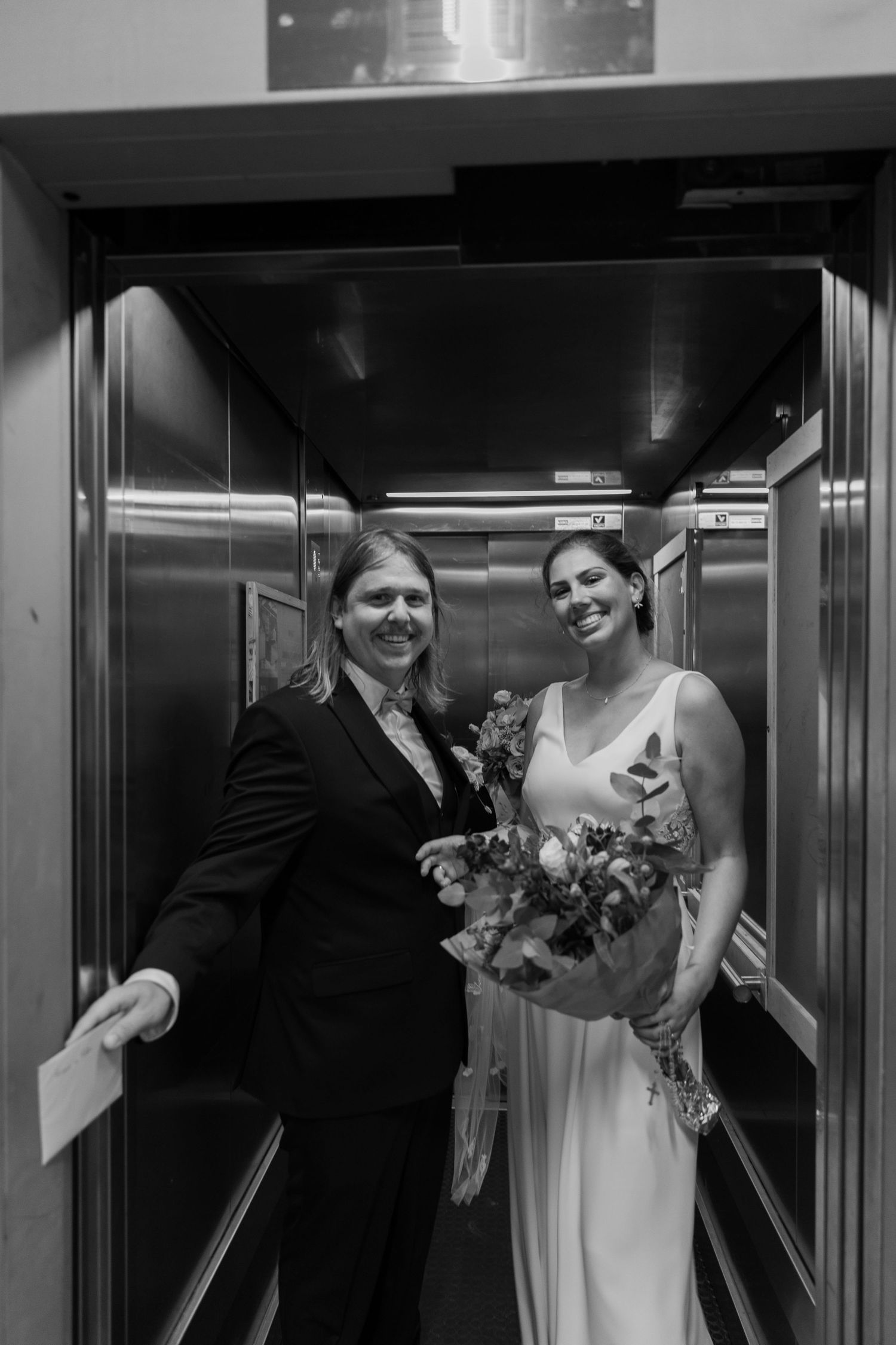 Bride and groom posing in elevator, bride holding bouquet, black and white wedding photo.