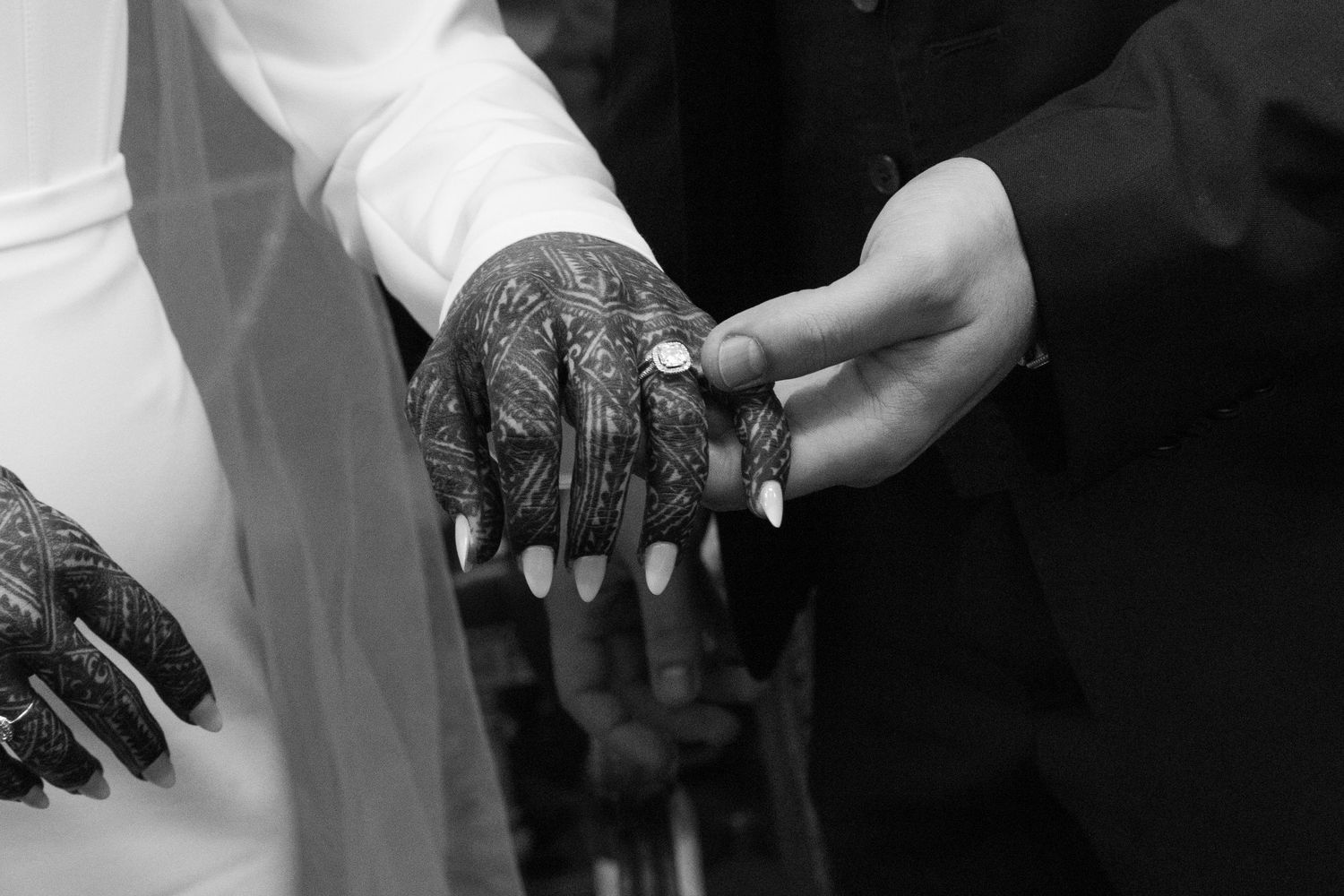 Black and white wedding photo of bride with henna hands receiving ring from groom.