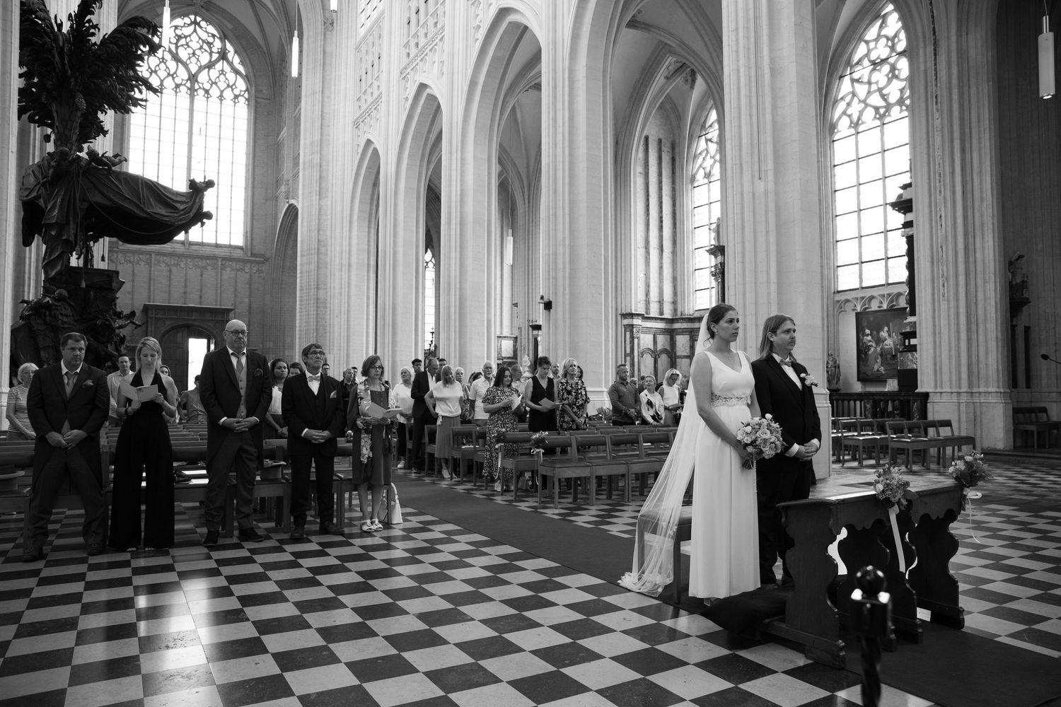 Black and white wedding ceremony photo inside a grand cathedral with checkered floors and gothic arches.