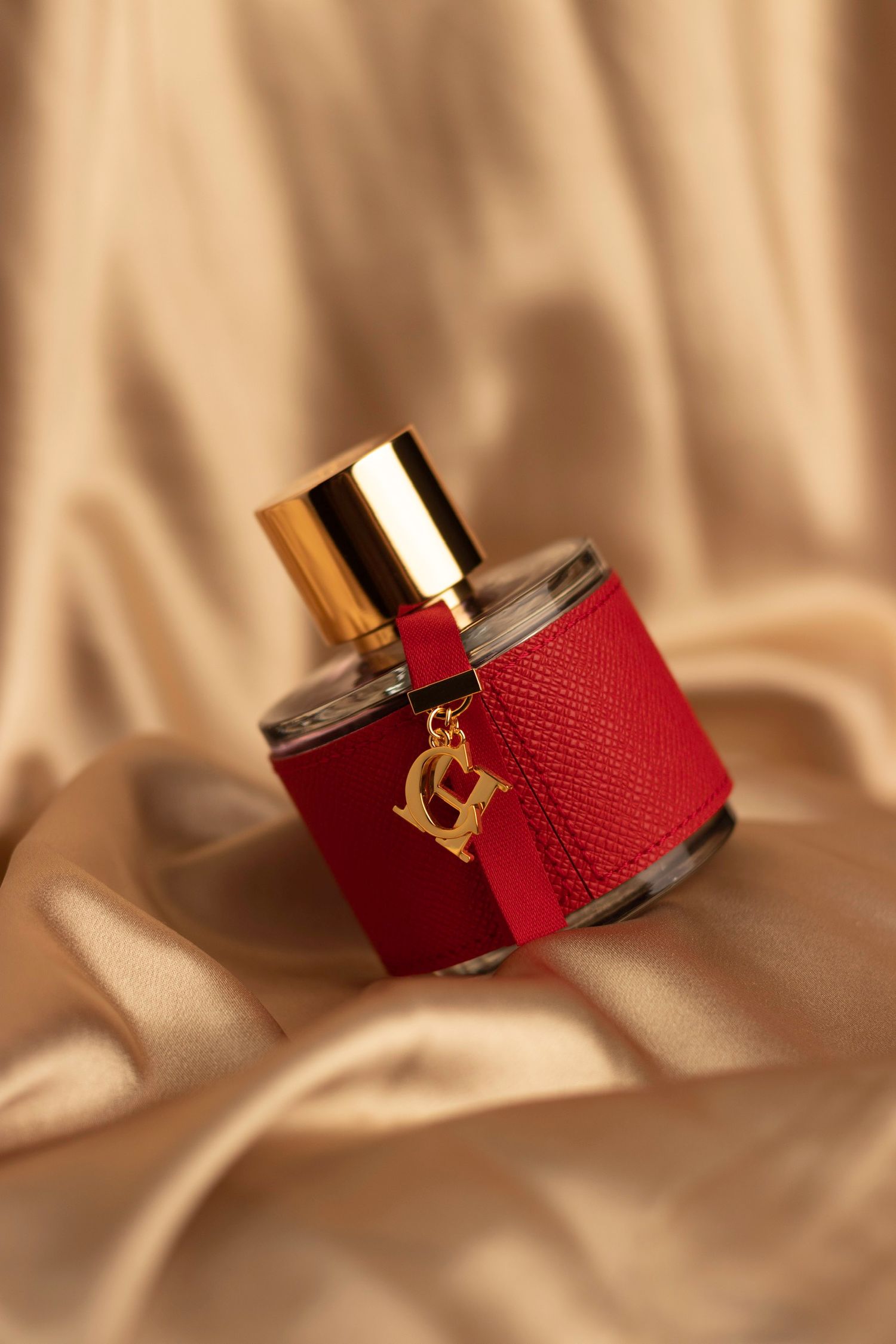 Carolina Herrera CH perfume bottle in red leather with gold charm on luxurious golden satin fabric.