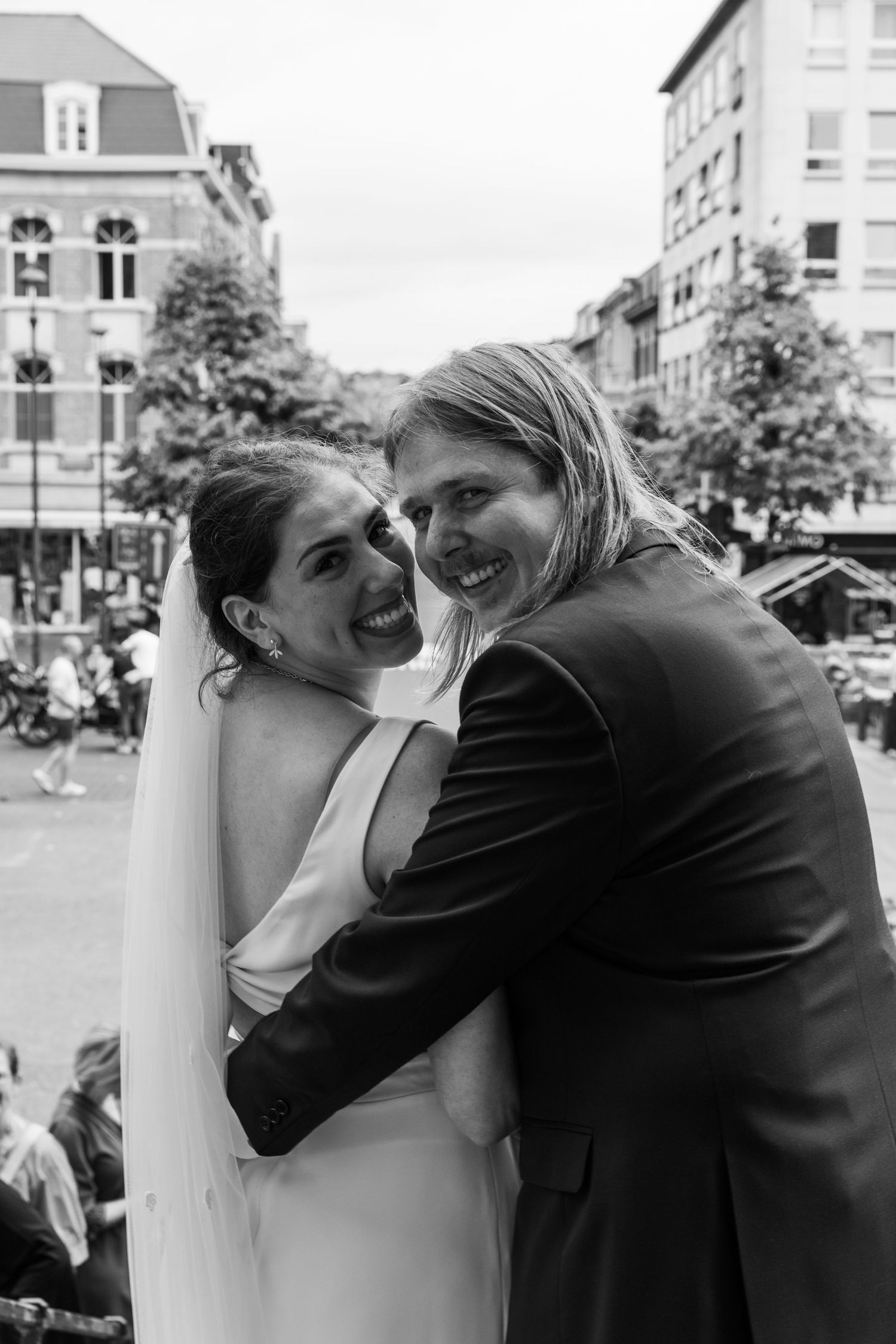 Black and white photo of smiling bride and groom embracing outdoors on their wedding day.