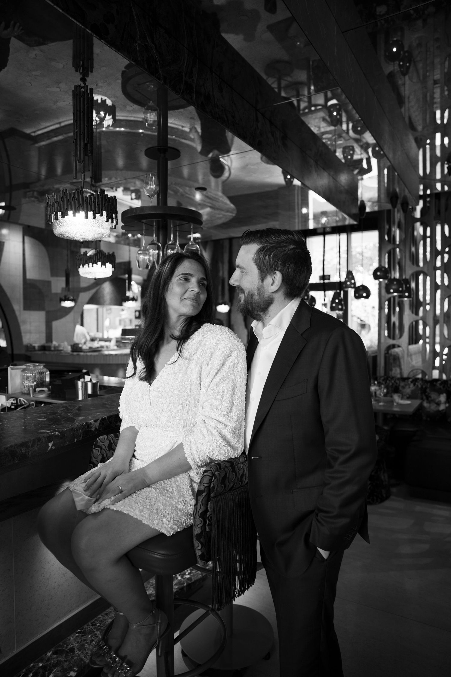 Black and white photo of a couple sharing a romantic moment at a bar, woman seated on stool, man standing close.
