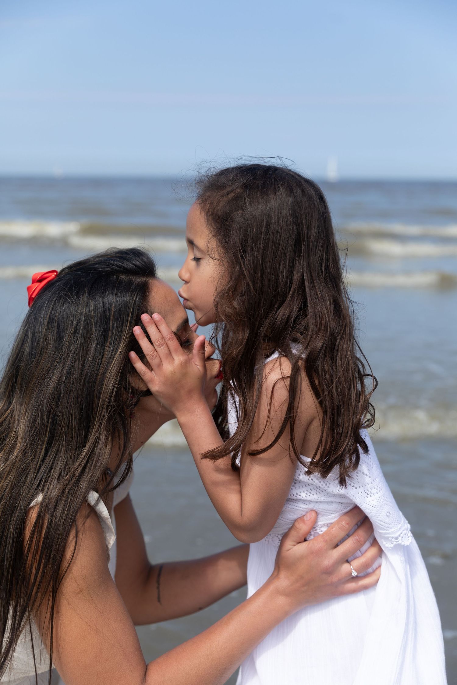 A mother and young daughter share a tender moment at the beach, with the child whispering in her mom's ear. photography brussels