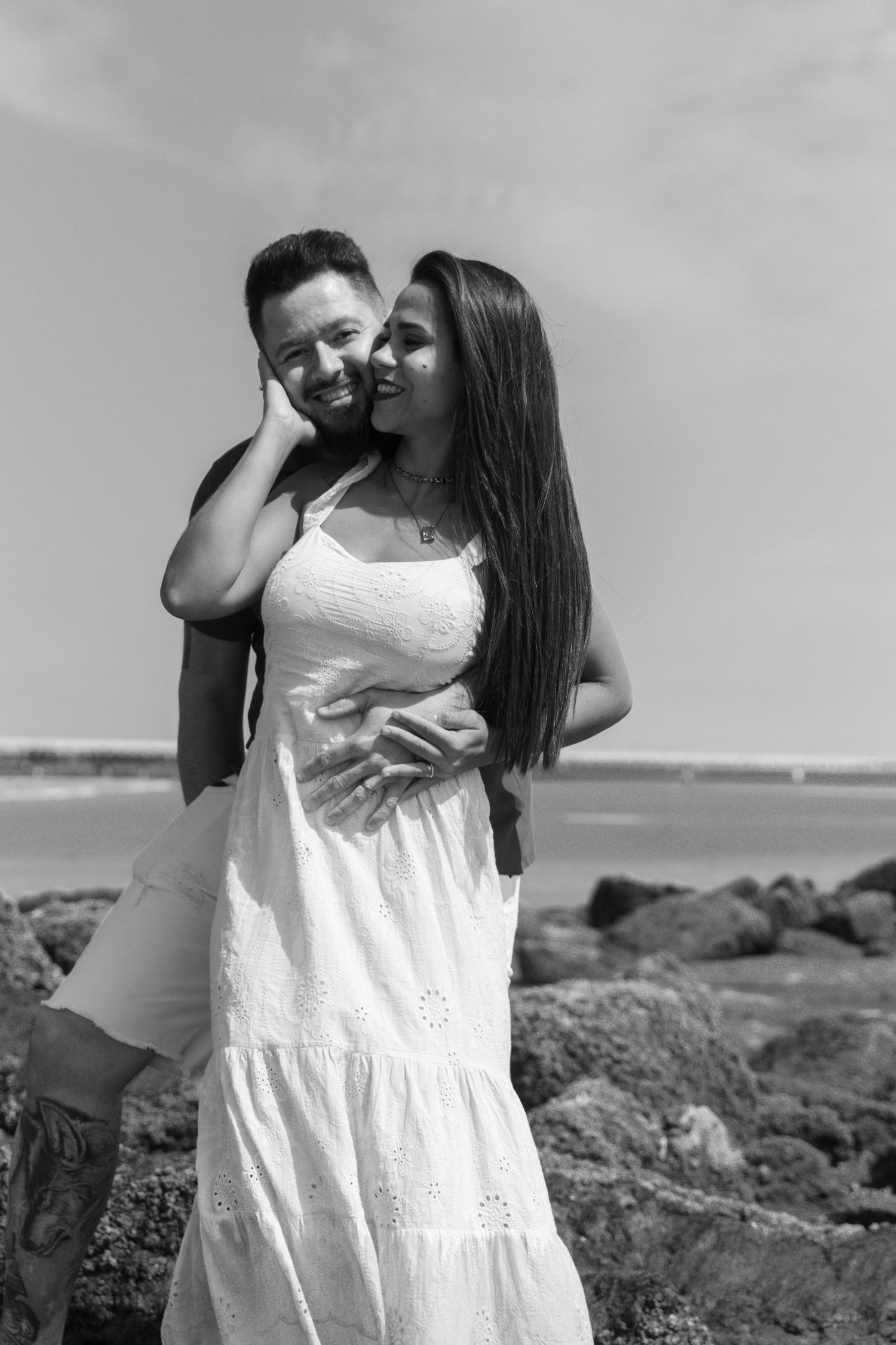 A happy couple embraces on a rocky beach in a black and white portrait photo. photography brussels