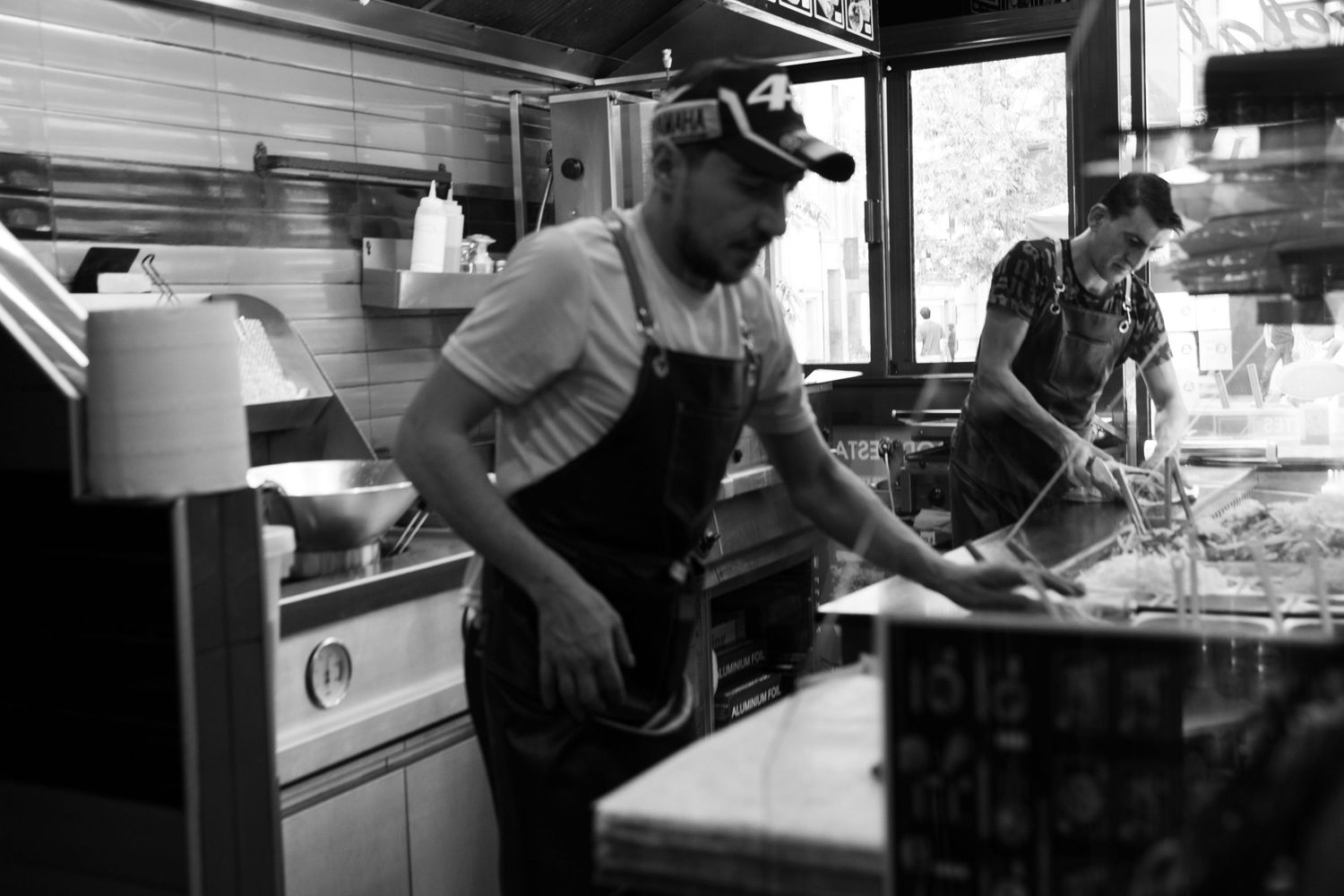 Two chefs working in a busy restaurant kitchen, preparing food in black and white photography.
