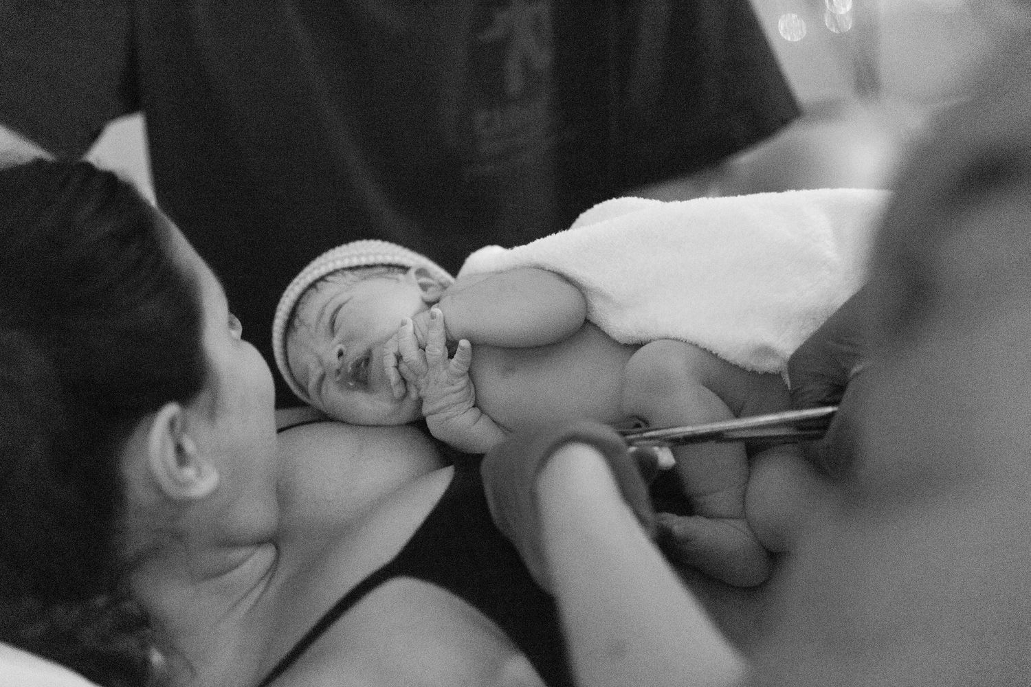 Black and white photo of a newborn baby being held and examined by medical professionals after birth.