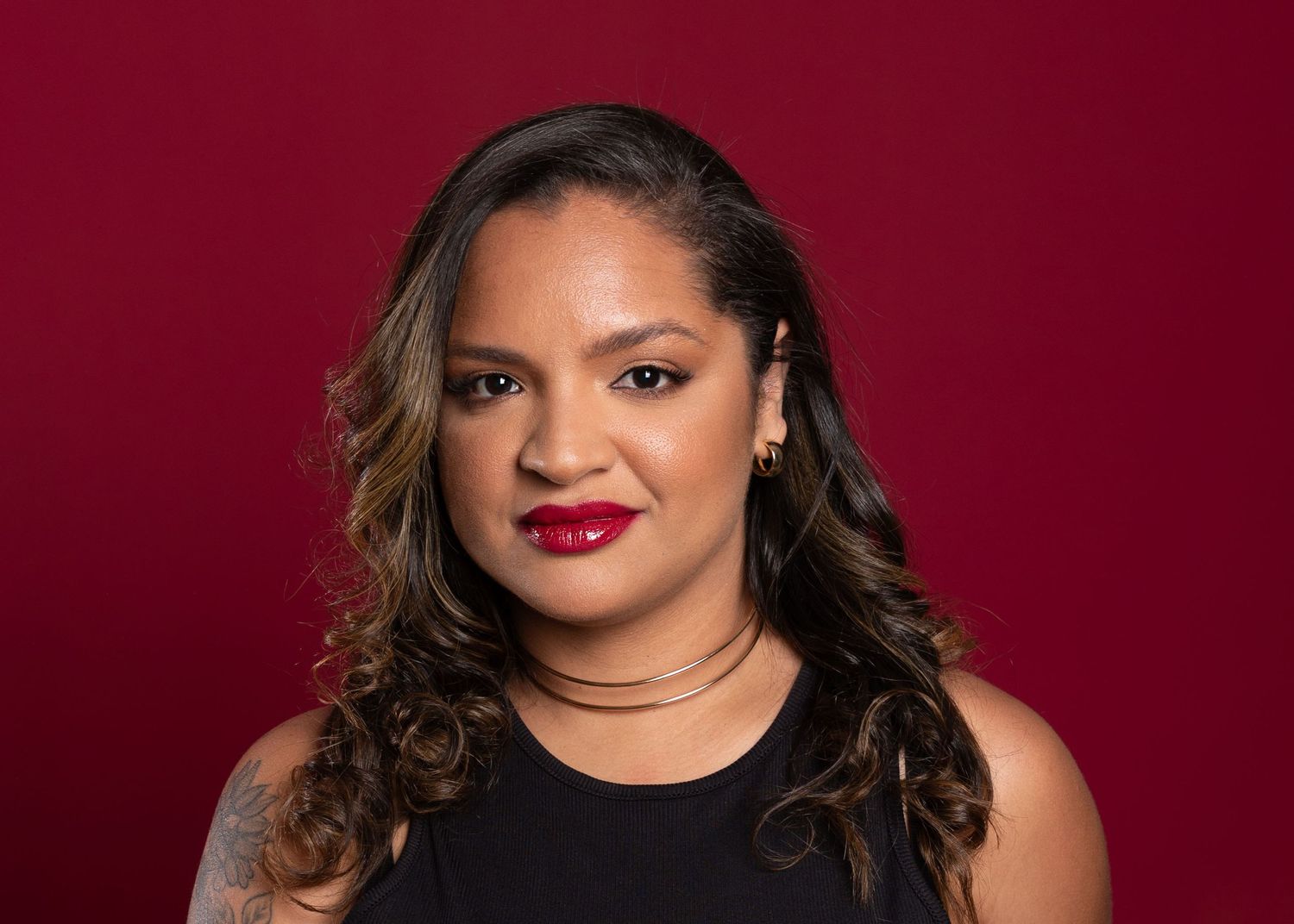 Professional headshot of a woman with long hair wearing a black top against a red background.