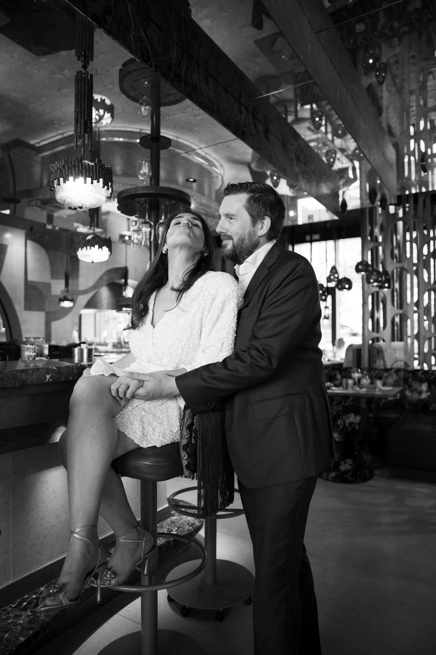 Black and white photo of an elegant couple embracing in a upscale restaurant bar setting.