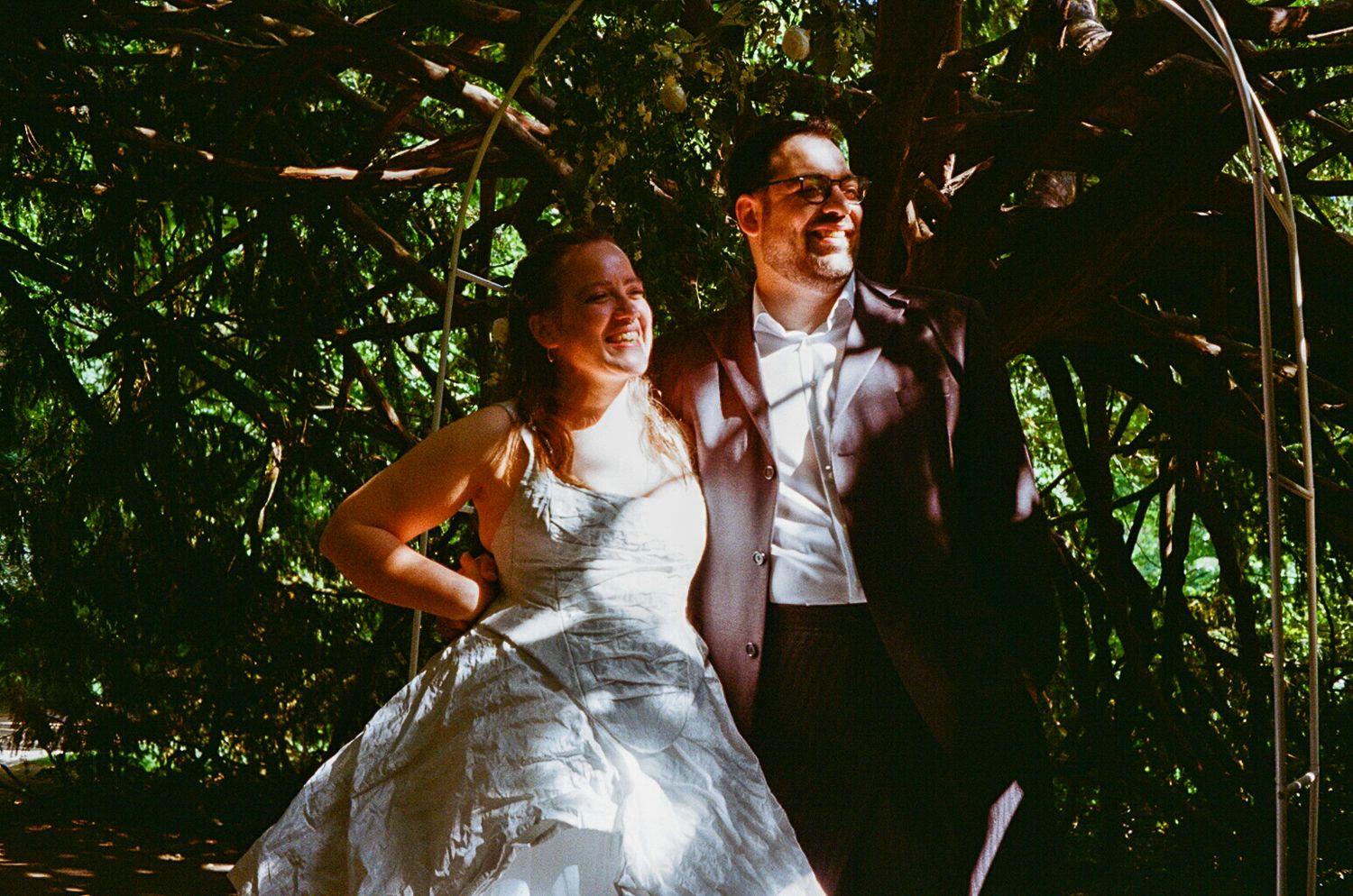 Happy bride and groom smiling together under a natural vine archway in an outdoor wedding setting.