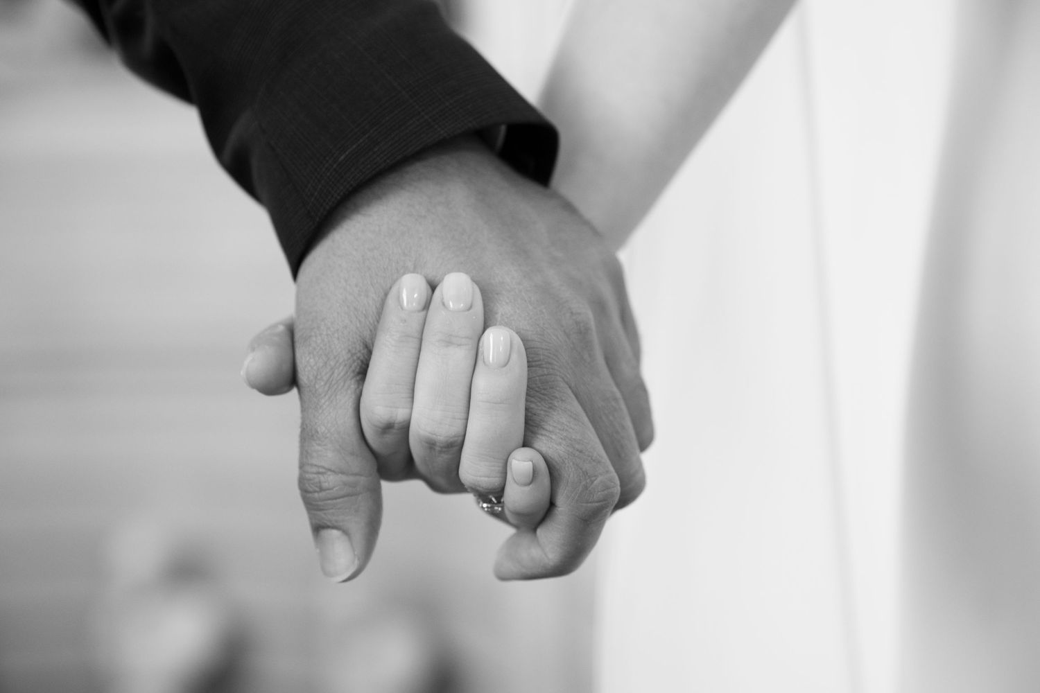 Black and white photo of a couple holding hands, showing a wedding ring, symbolizing love and commitment.