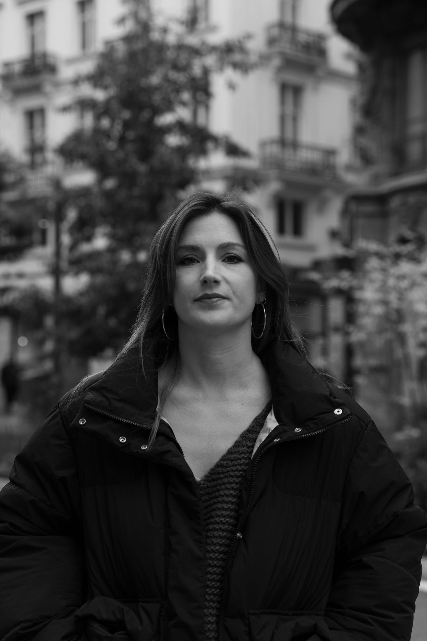 Black and white portrait of a woman in a black jacket standing outdoors with blurred urban background.photography brussels