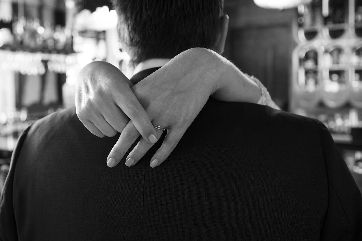Black and white photo of a woman resting her hand on a man's shoulder at a bar.