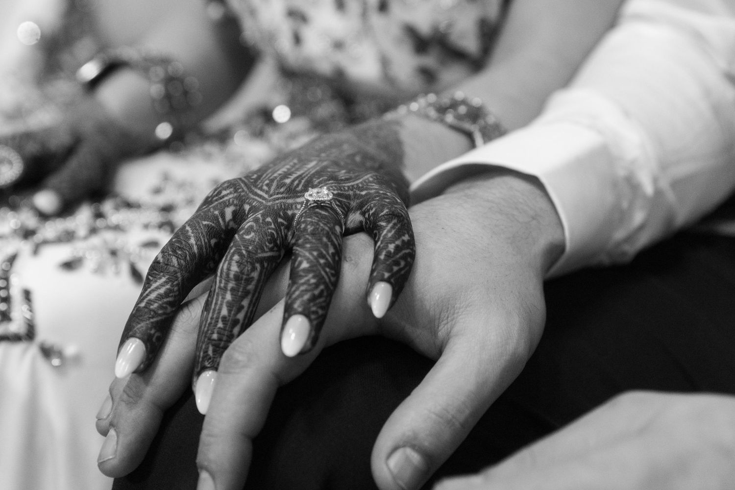 Black and white photo of a couple holding hands, bride adorned with intricate henna mehndi design on her hand.