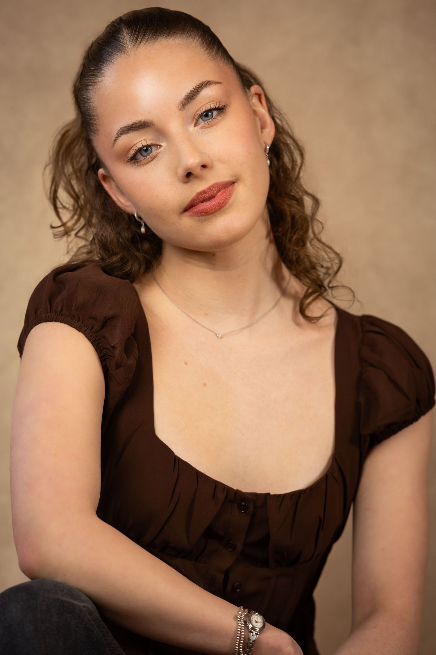Studio portrait with brown backdrop showing elegant poses in a dark brown dress and natural makeup.