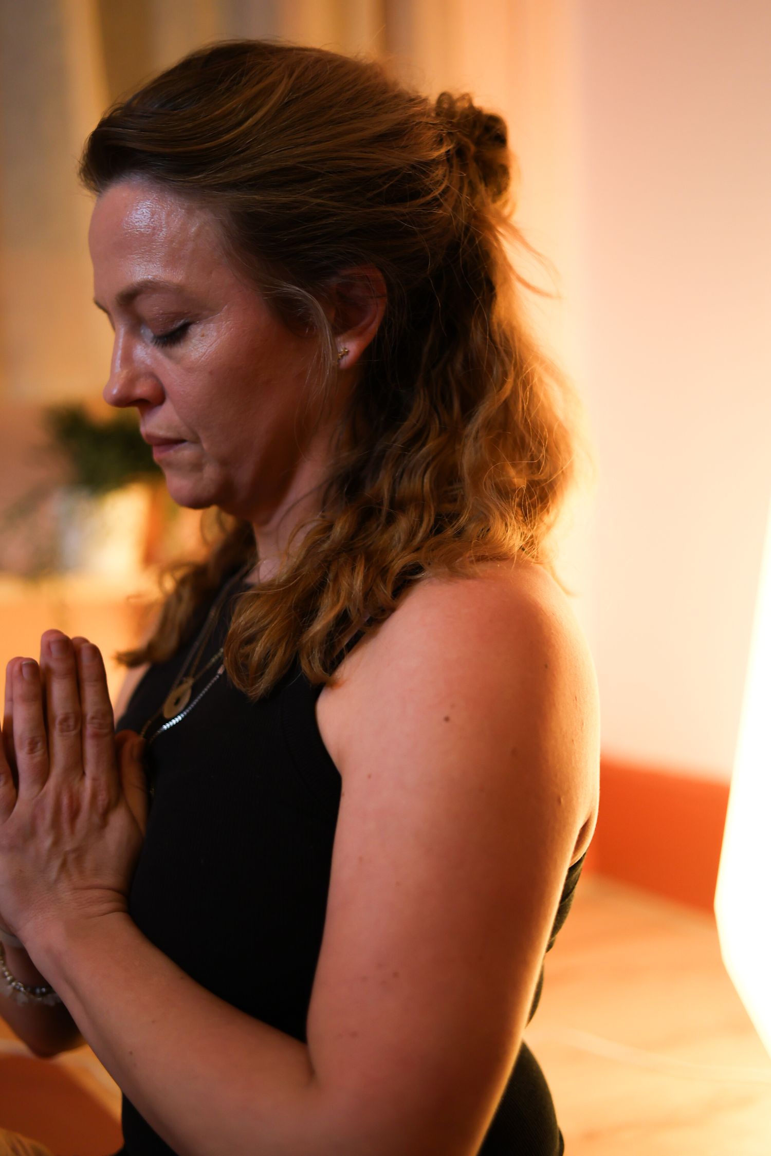 A person in a black tank top meditates with hands pressed together in prayer position during a peaceful moment.