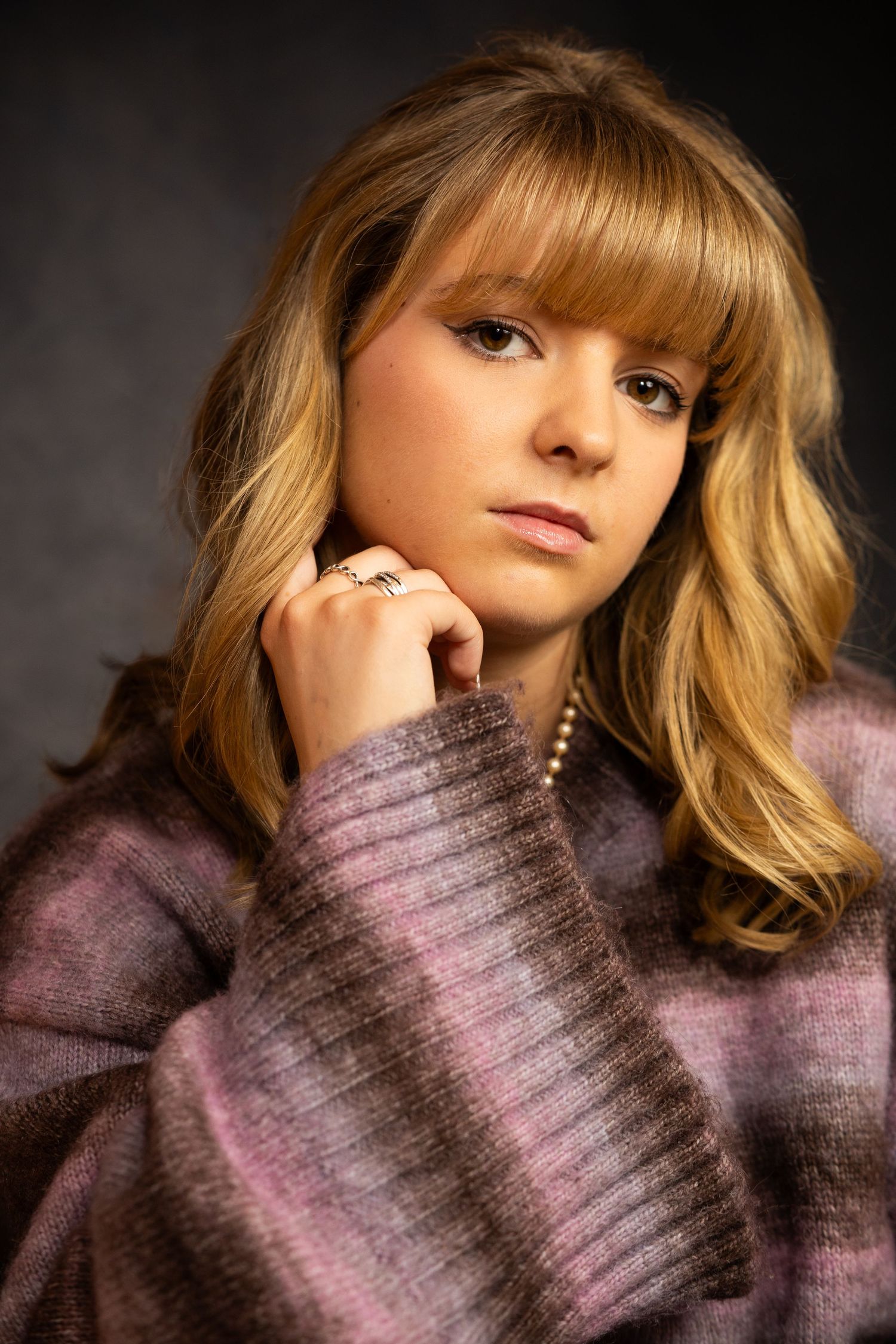A series of artistic portraits showing someone wearing a cozy purple sweater against a dark background.