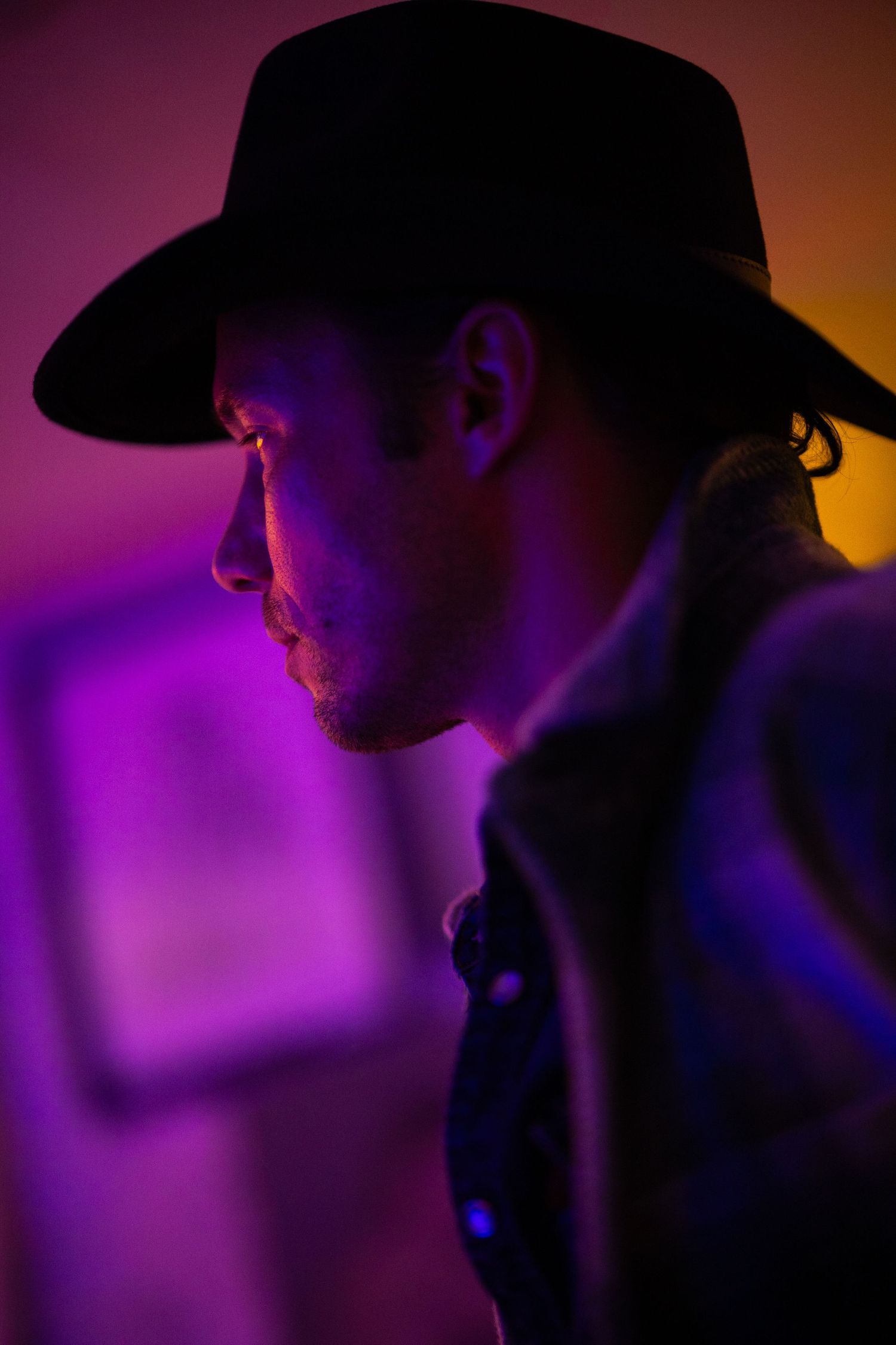 Silhouetted profile against vibrant purple and orange gradient lighting creates a dramatic atmospheric mood.