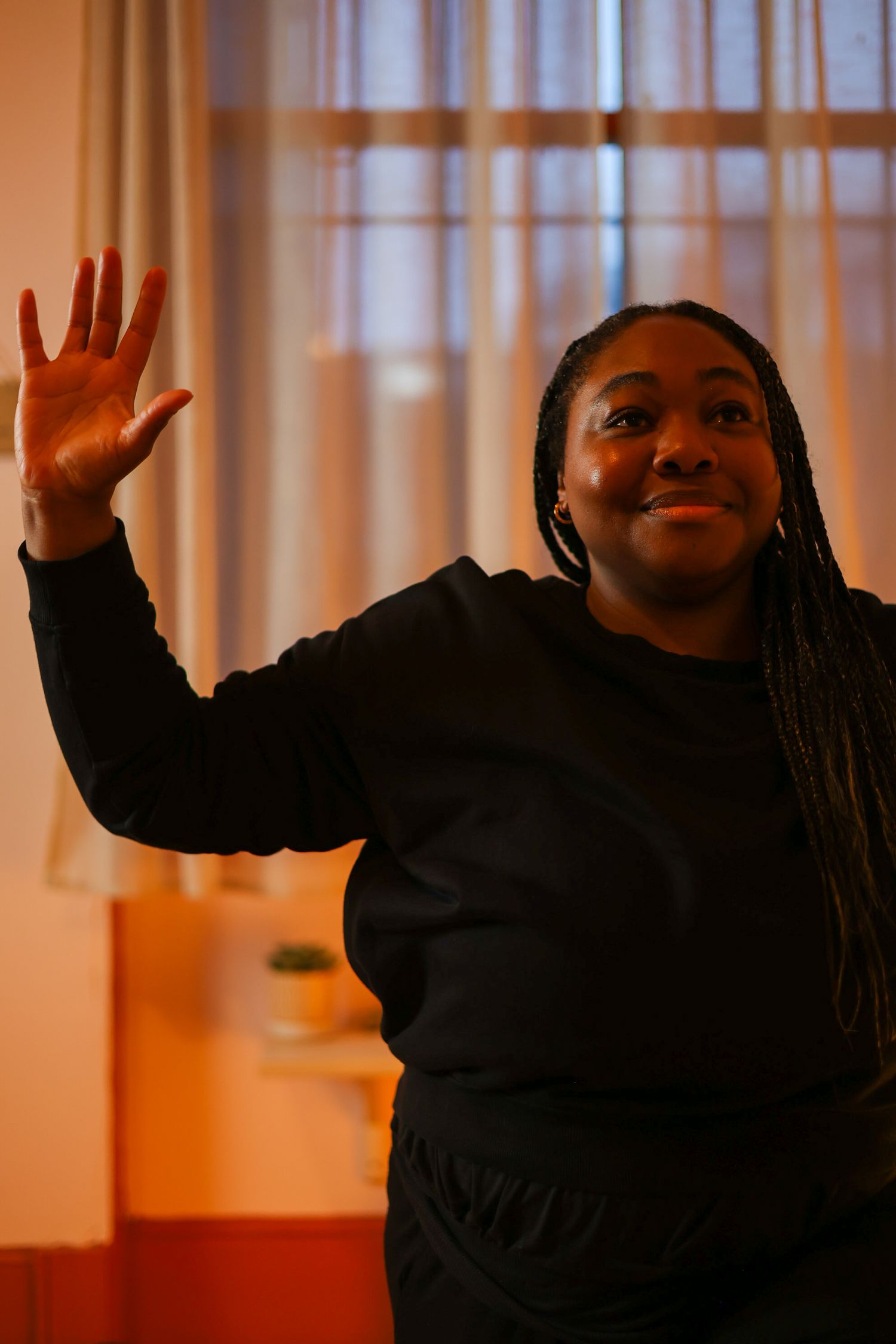A person in a black sweater waves and smiles with joyful expressions in a series of four connected photos.
