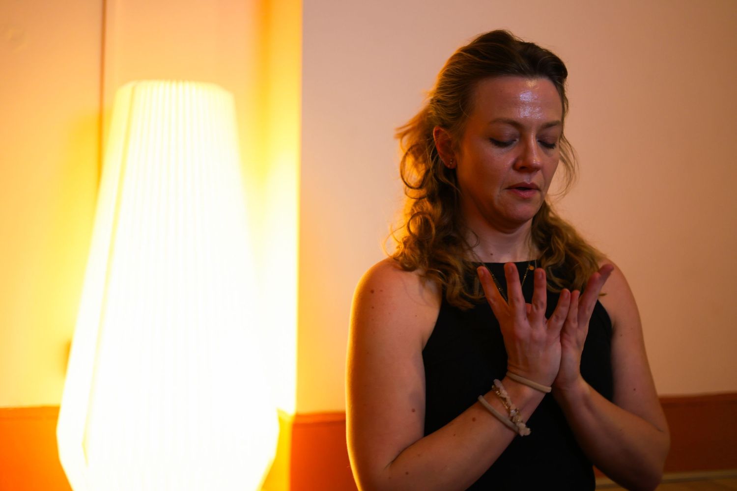 A person in black clothing sits in a dimly lit room with warm orange lighting creating a contemplative mood.