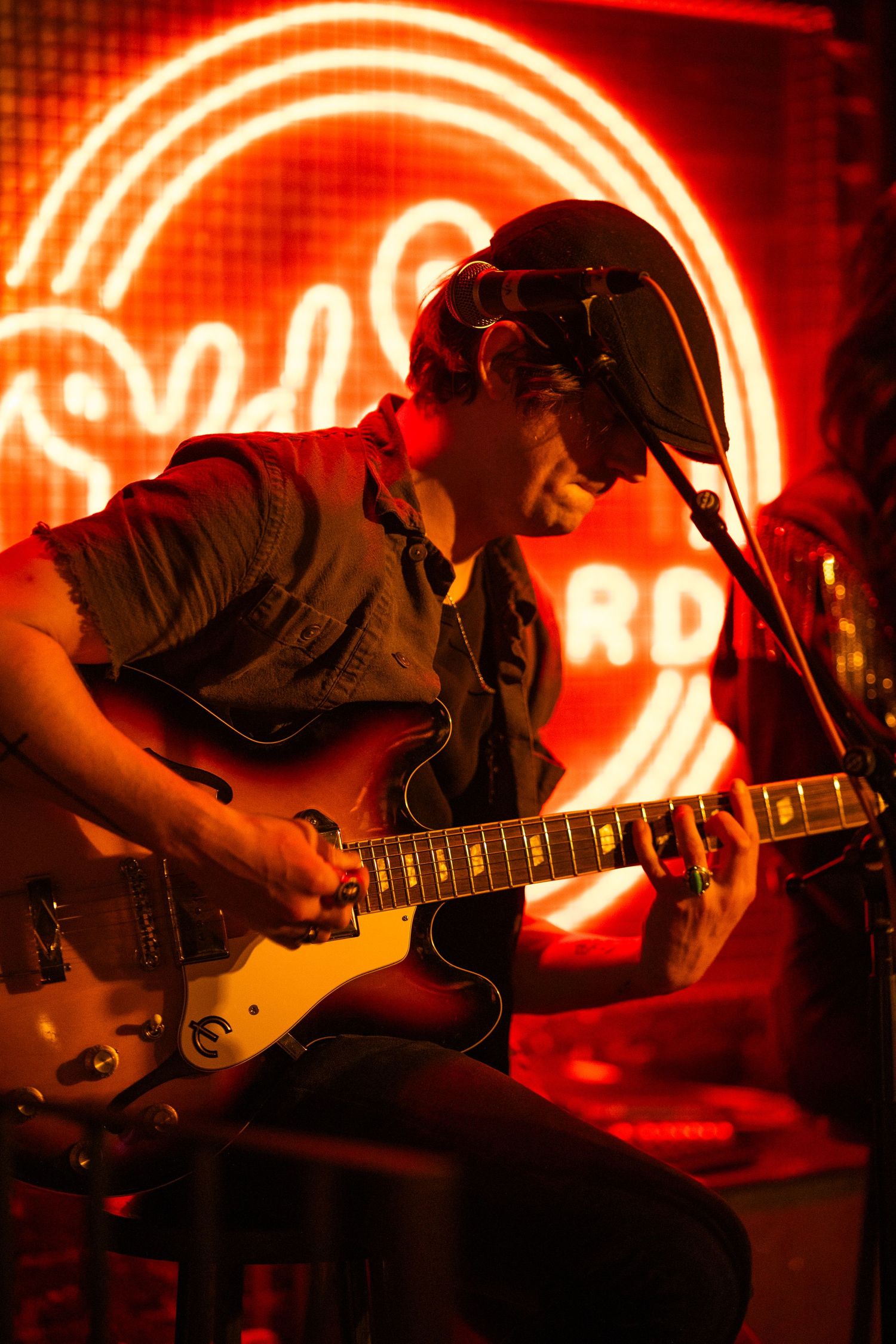 Musician performs with electric guitar against glowing red neon lights in dramatic silhouette at live music venue.