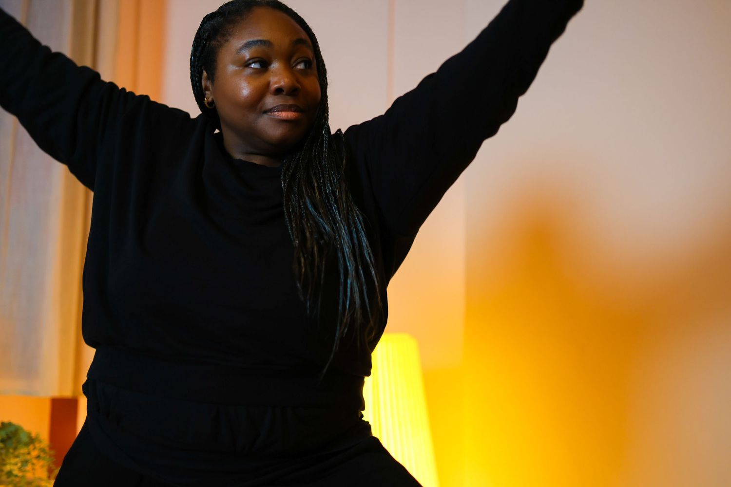 A person in a black sweater raises their arms joyfully against a warm orange-lit background.
