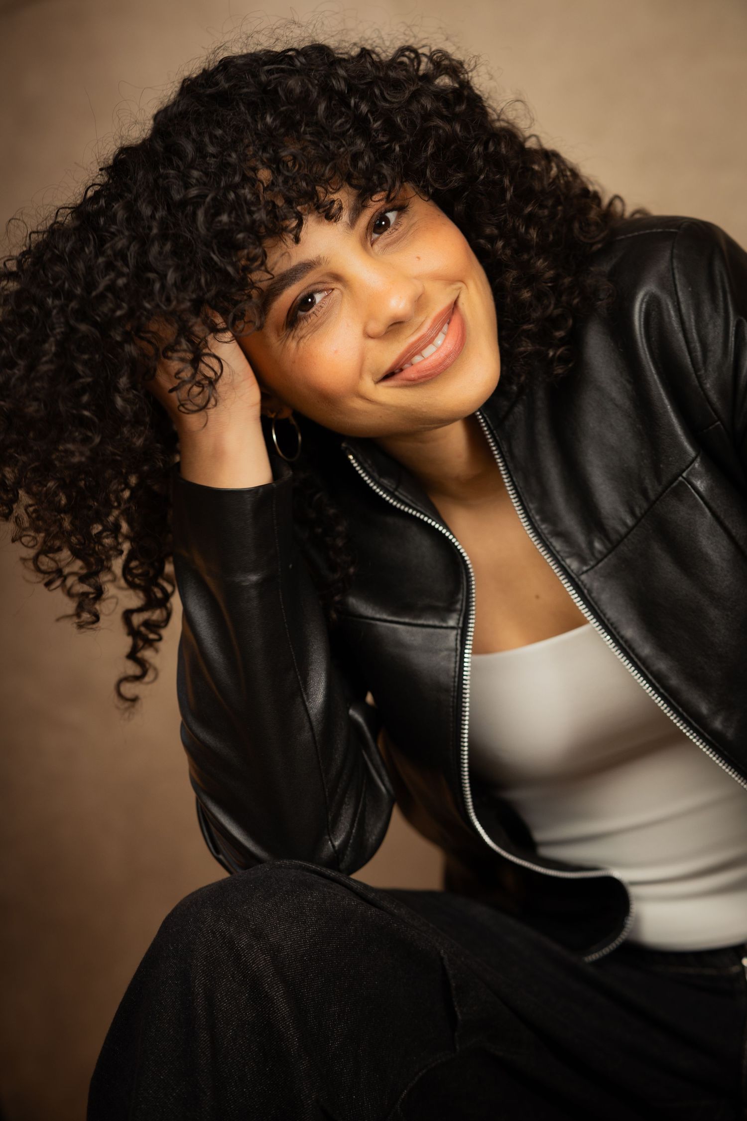 Portrait series showing person with natural curly hair and black leather jacket against warm brown background.