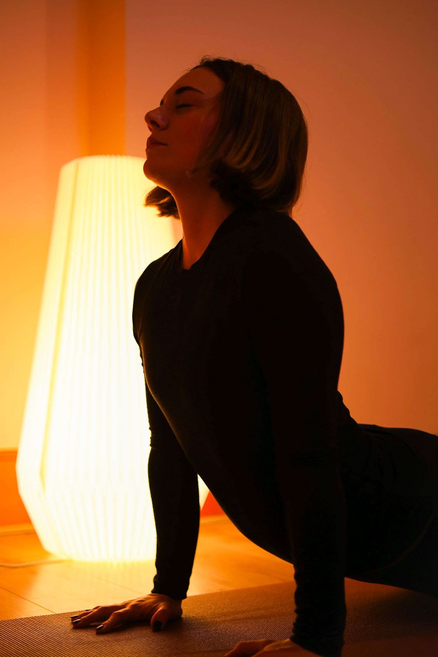 A silhouetted figure performs a graceful dance movement against a warm orange backlit wall.