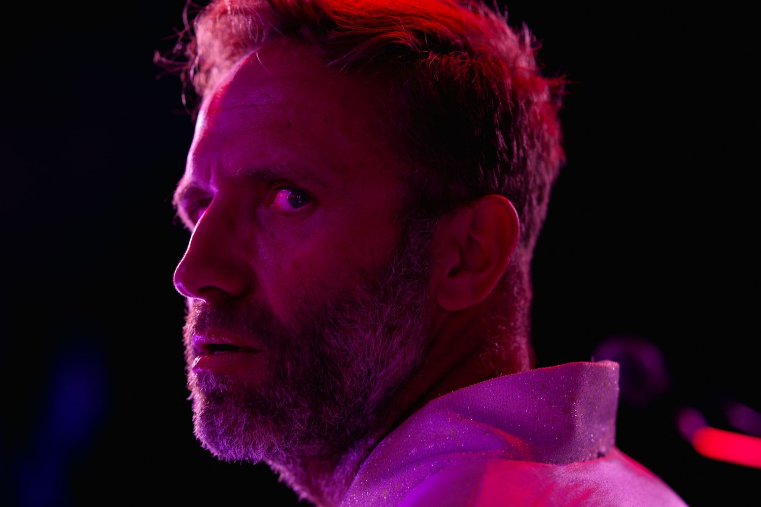A silhouetted profile view of someone illuminated by pink and purple stage lighting against a dark background.