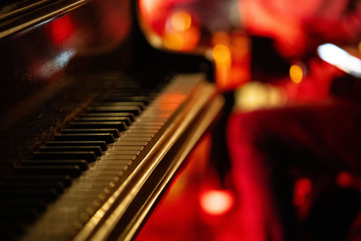 Close-up view of piano keys with red and gold bokeh lights creating a festive holiday atmosphere.