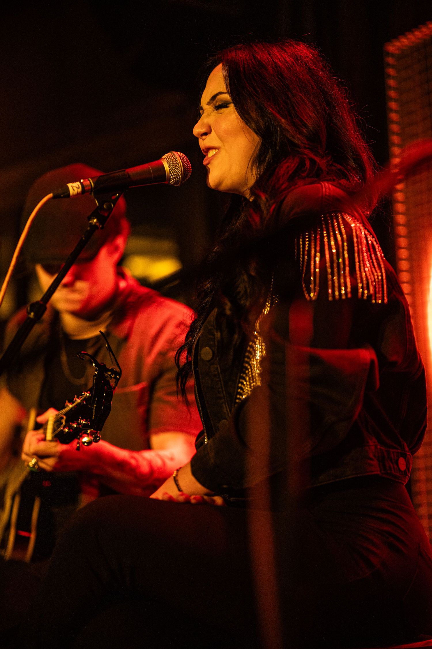 A singer performs on stage in dramatic red lighting with a microphone during a live concert performance.