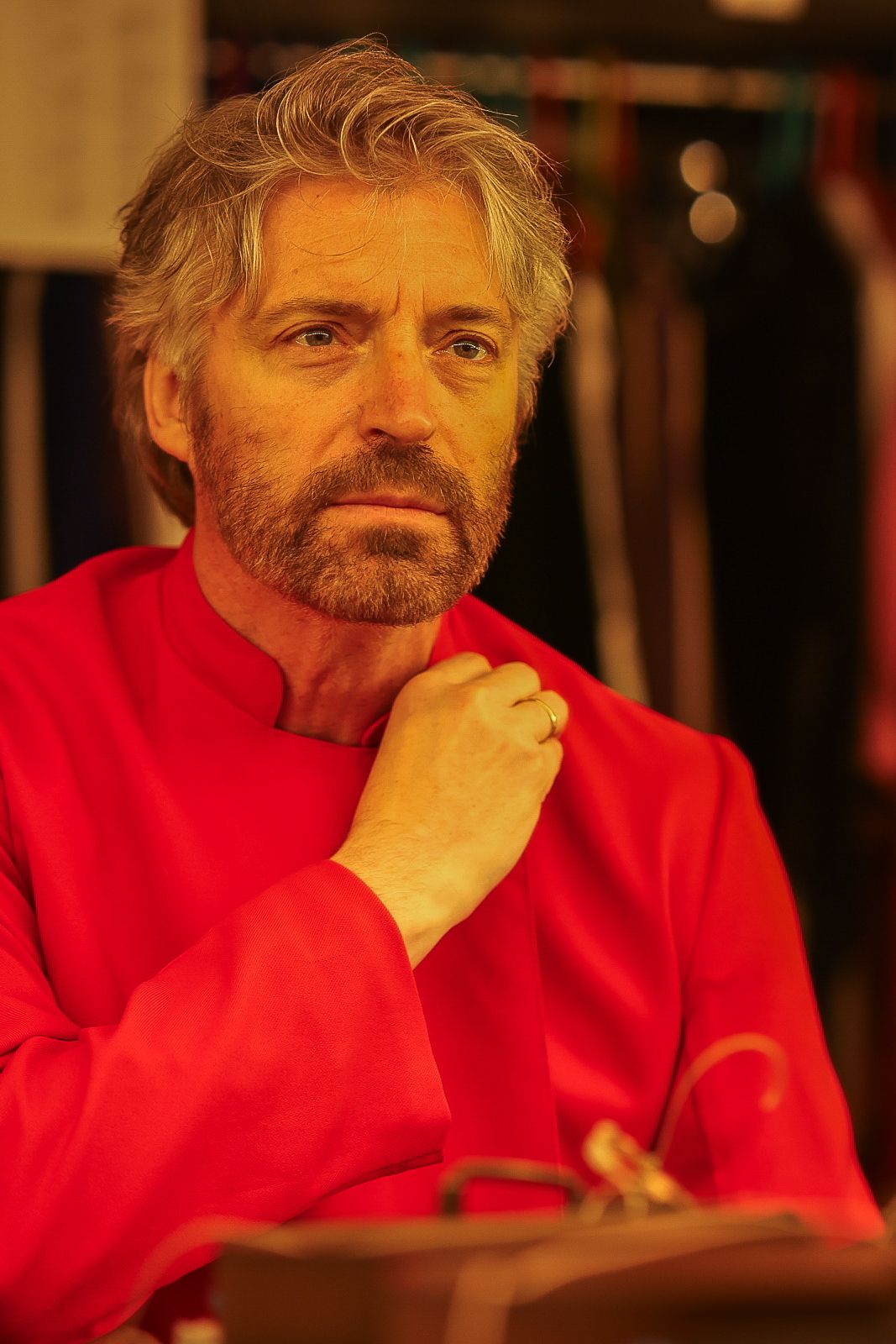 A person in a bright red sweater sits thoughtfully with their hand on their chin in warm lighting.