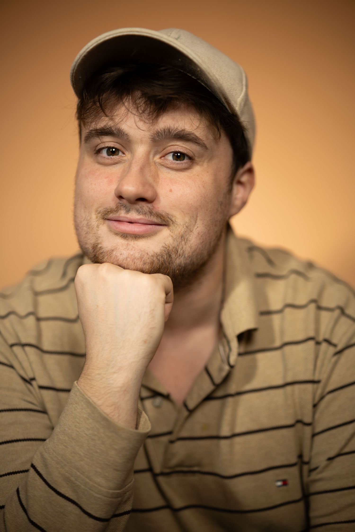 Portrait of someone in a striped shirt and baseball cap with hand resting on chin.