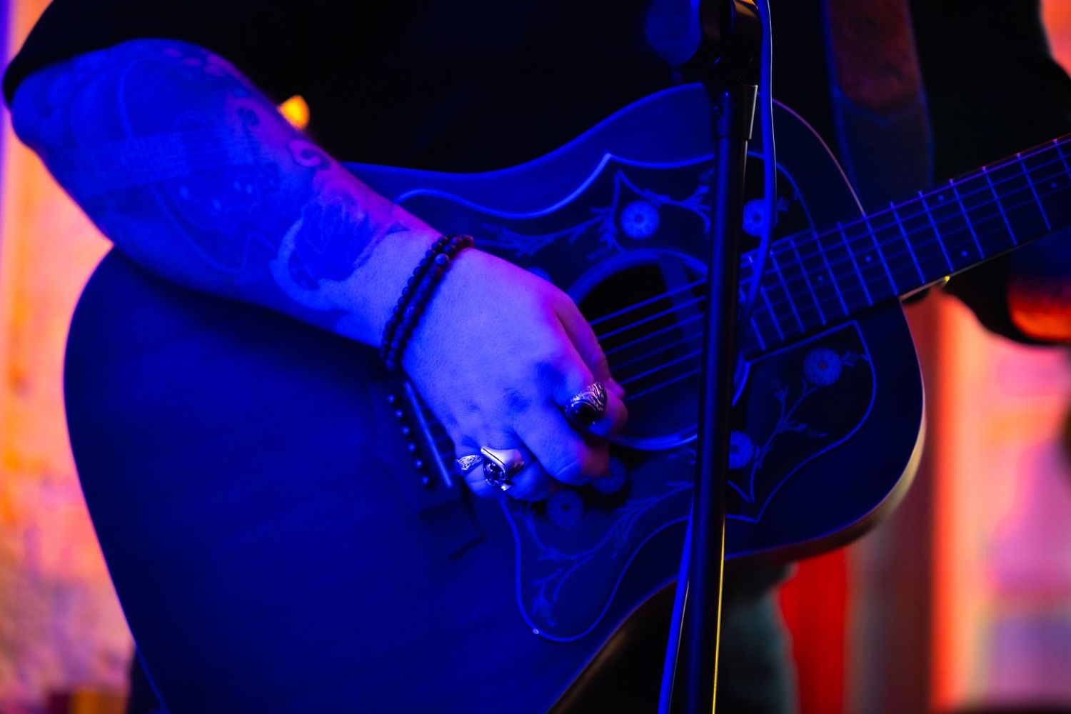 A guitarist performs on stage with dramatic blue and red lighting creating a moody concert atmosphere.