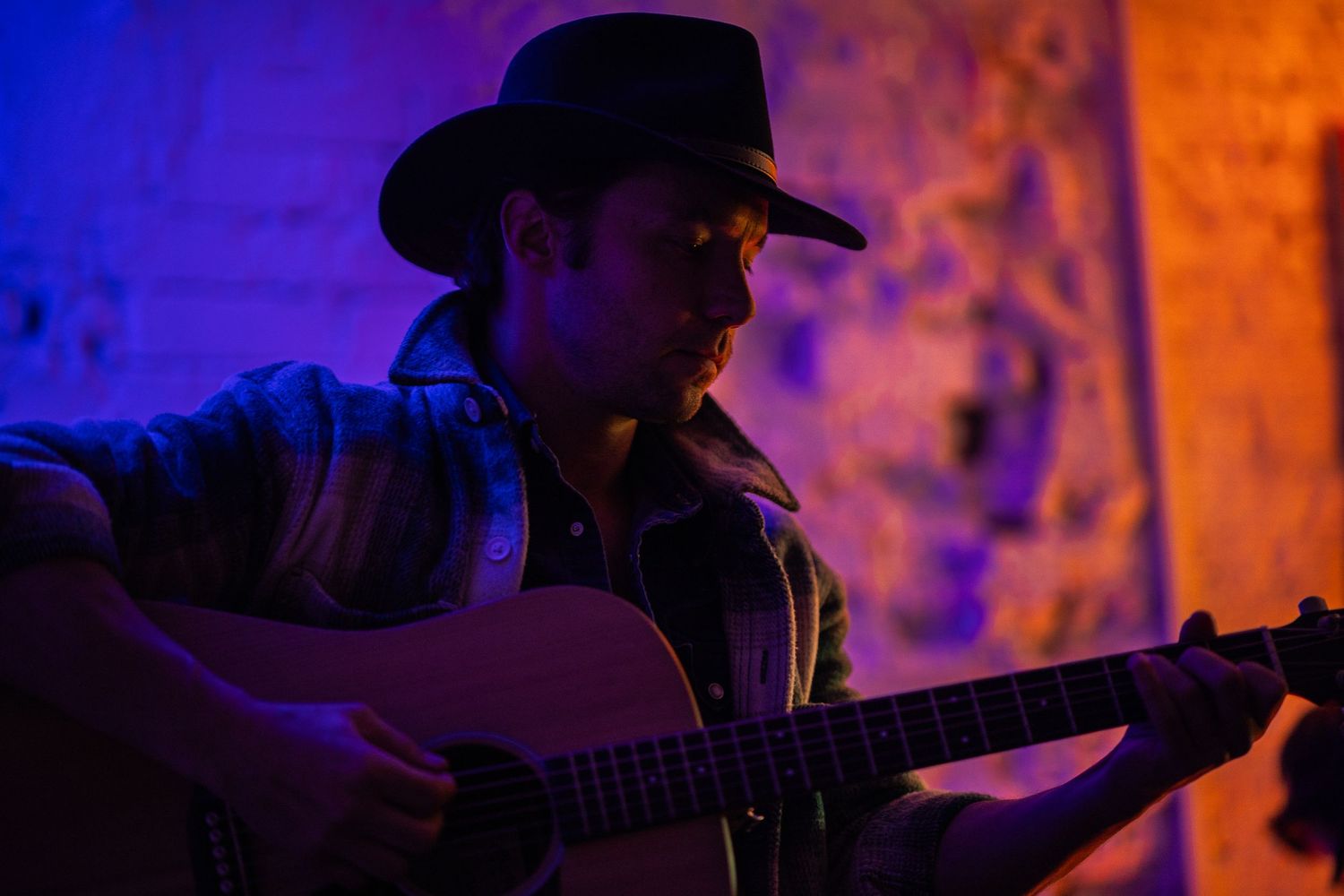Silhouetted musician plays guitar on stage with vibrant orange and blue lighting effects in the background.