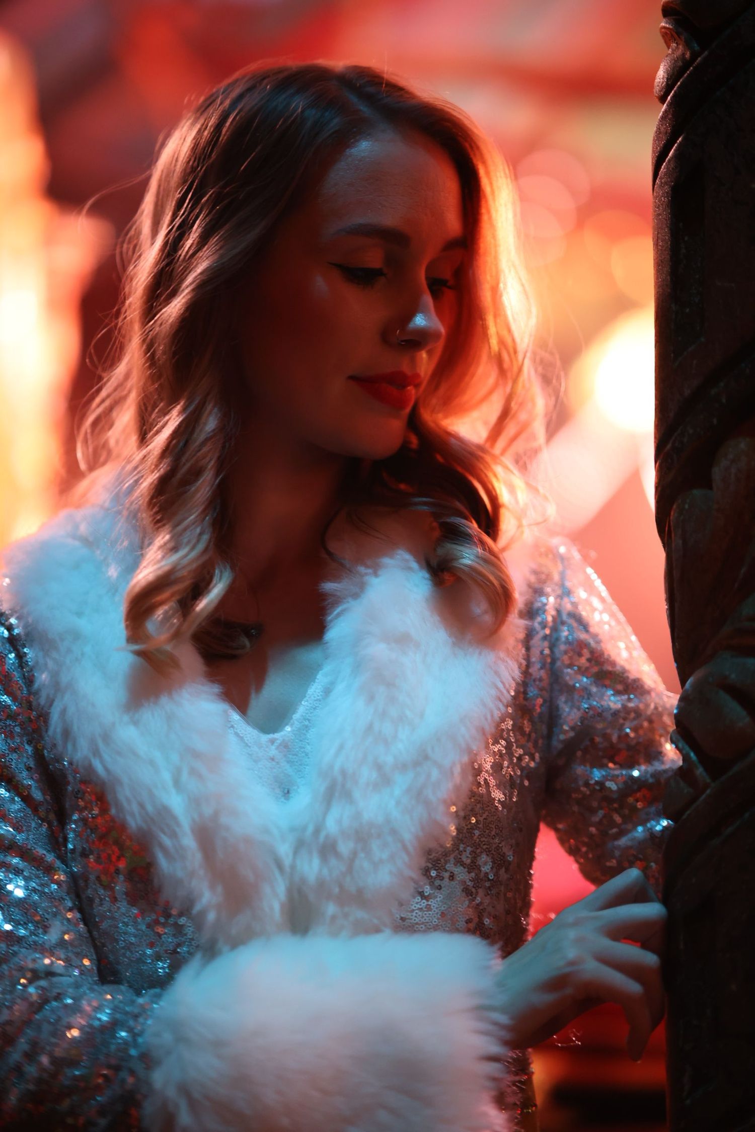 A woman in sequins poses dramatically with swirling white smoke effects against a red-tinted background.