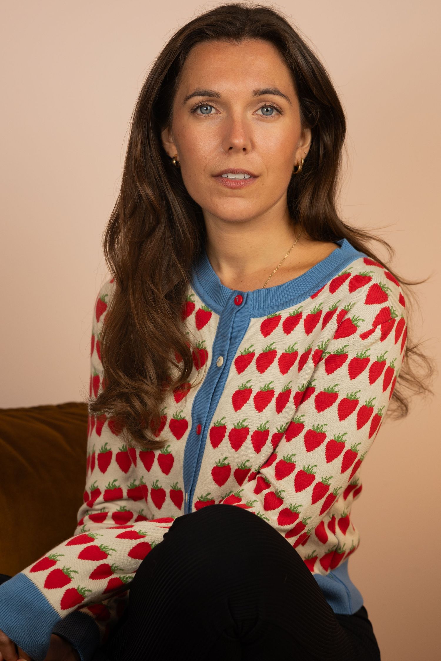 Woman wearing a vintage-inspired cream sweater with red heart pattern and blue trim details in studio setting.