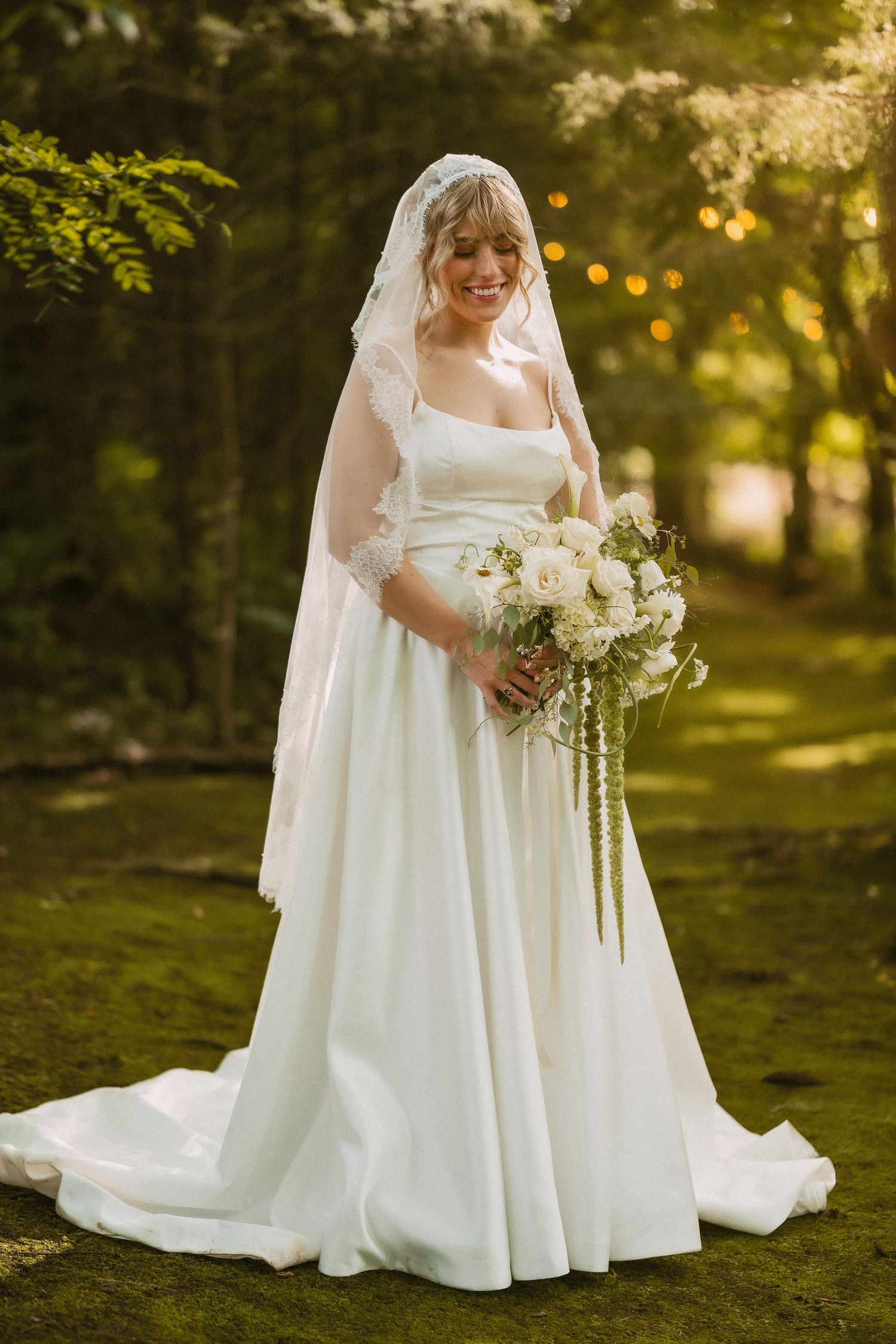 A flowing white wedding dress is displayed in a sunlit garden setting with ethereal lighting and cascading floral bouquet details.
