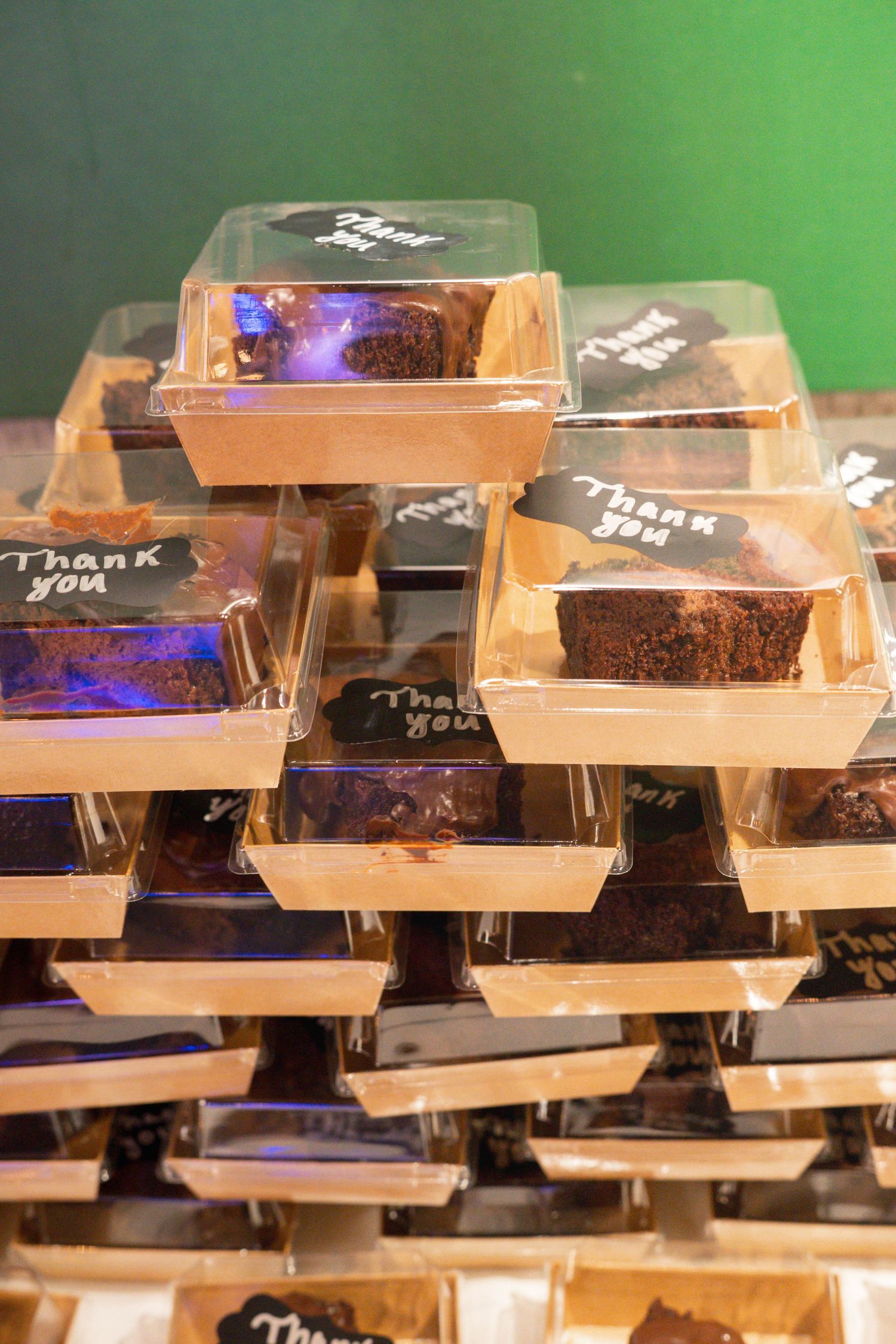 Stacked wooden boxes containing chocolate brownies with 'Thank You' written on them displayed against a green background.