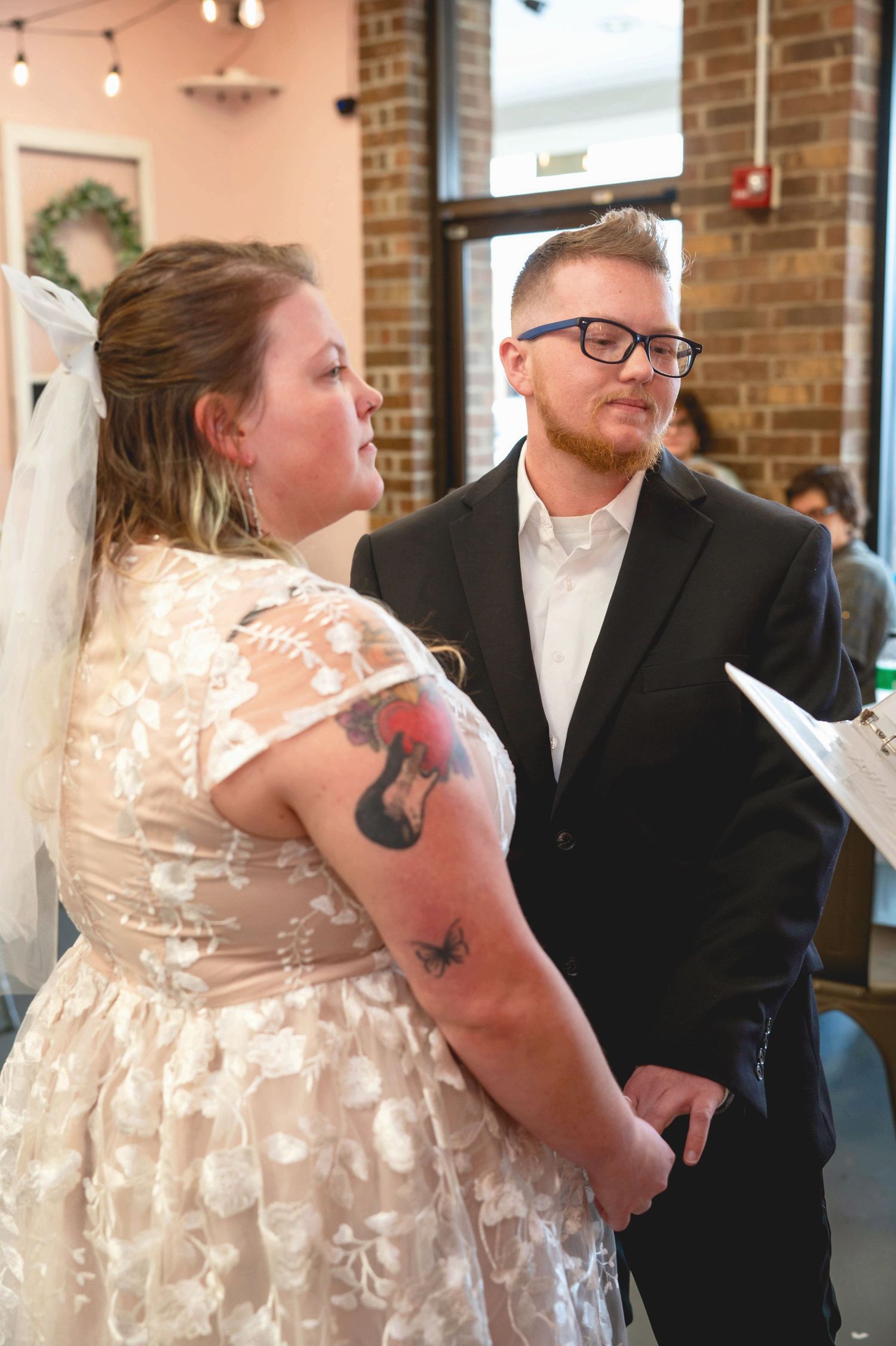 A couple in wedding attire share an intimate moment in a rustic brick-walled venue.