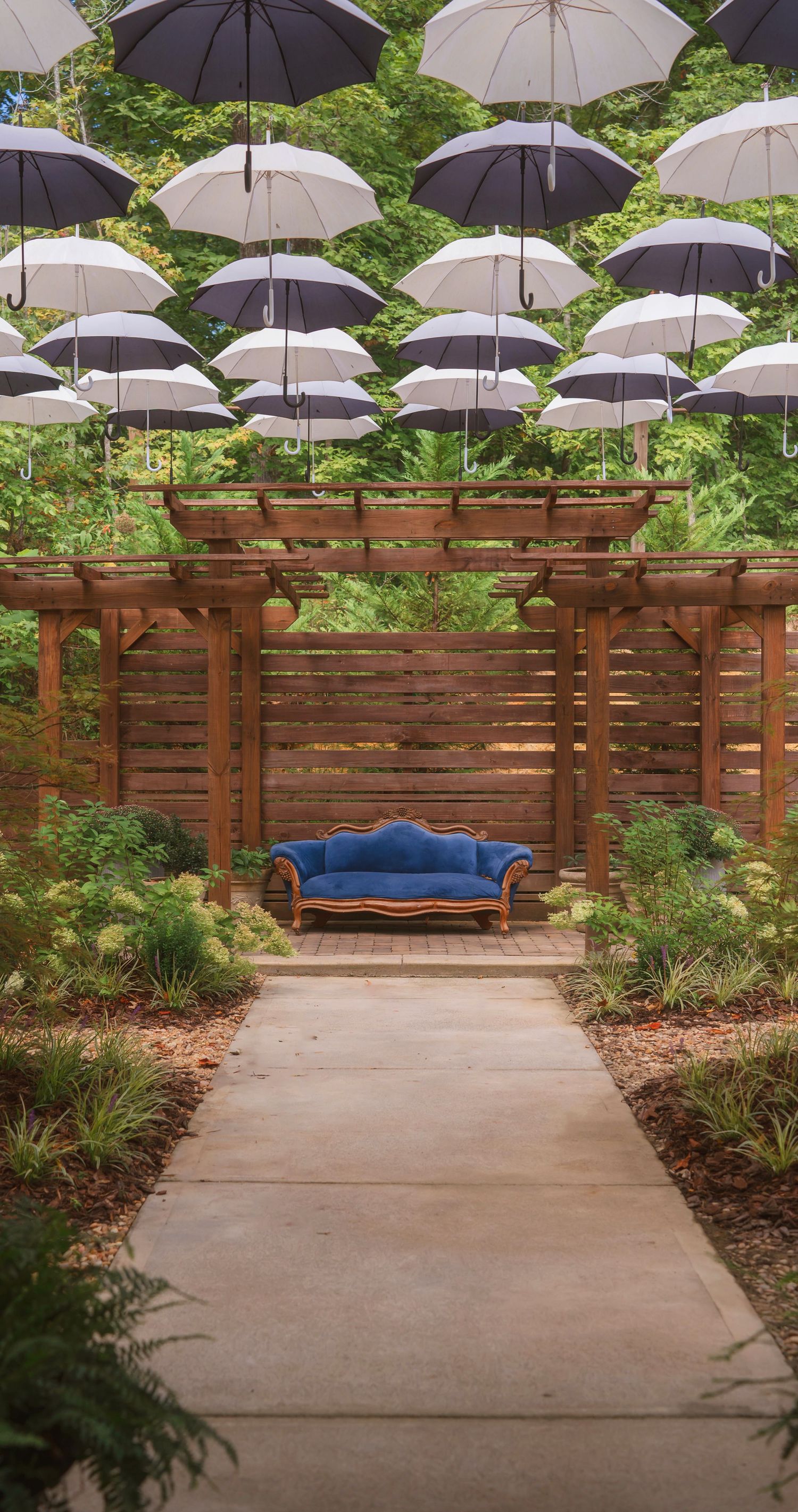 Artistic outdoor seating area with floating white umbrellas over a concrete patio and wooden privacy wall surrounded by plants.